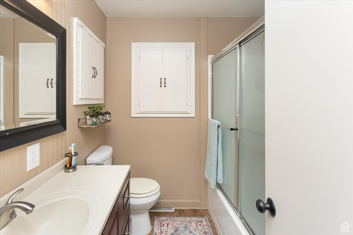 Full bathroom with vanity, tile patterned floors, toilet, and combined bath / shower with glass door