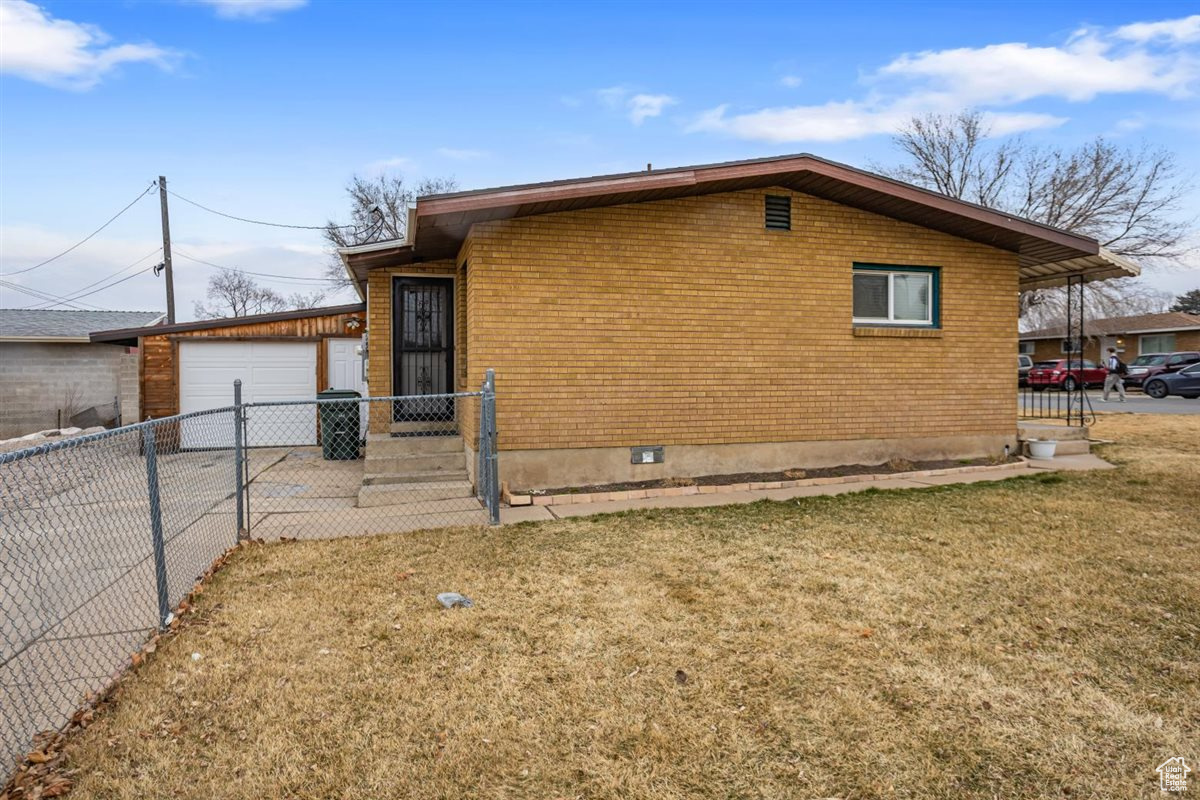 Exterior space with brick siding, a yard, fence, driveway, and an outdoor structure