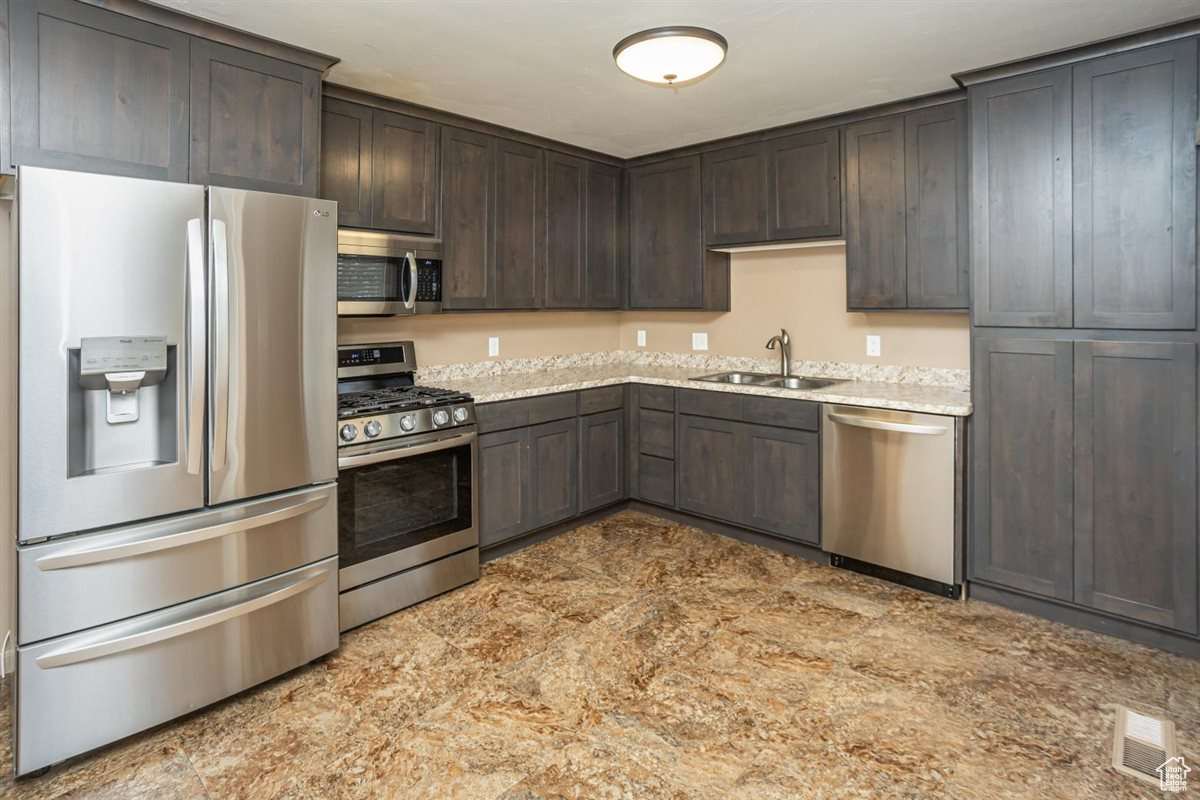 Kitchen with light stone counters, stainless steel appliances, a sink, visible vents, and dark brown cabinets