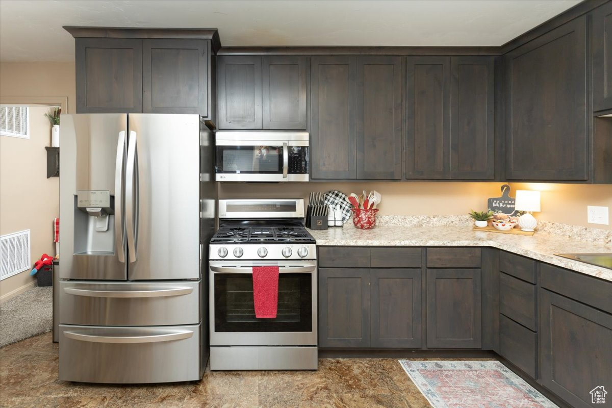 Kitchen with light stone counters, dark brown cabinetry, and appliances with stainless steel finishes