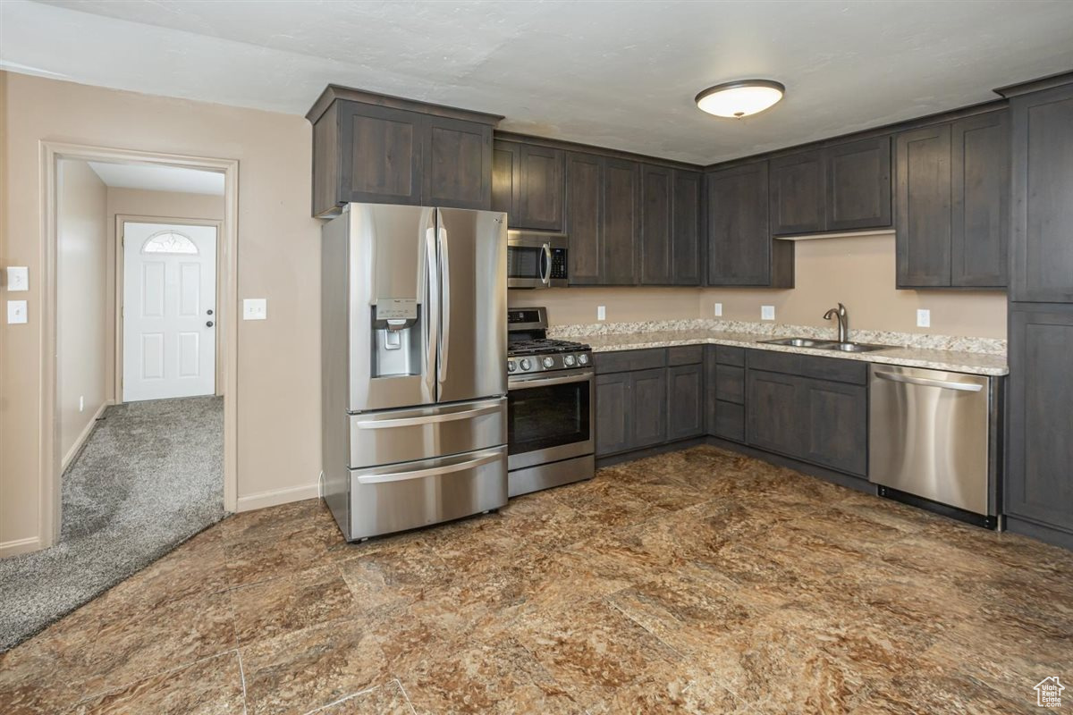 Kitchen with a sink, baseboards, dark brown cabinets, appliances with stainless steel finishes, and dark colored carpet