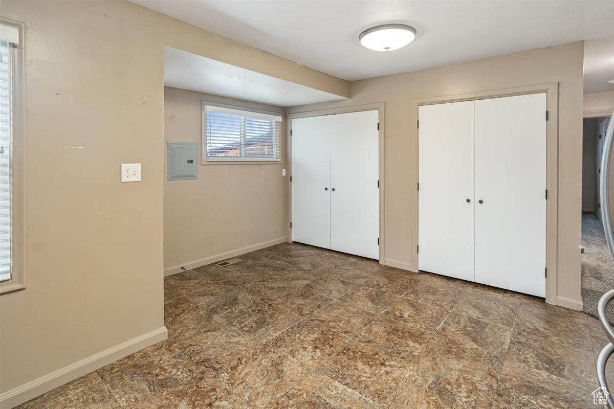 Unfurnished bedroom with baseboards, stone finish floor, electric panel, and multiple closets