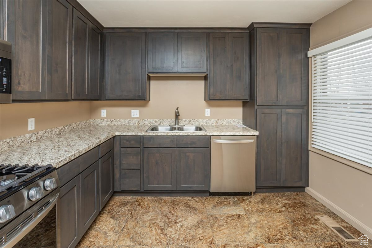 Kitchen featuring visible vents, appliances with stainless steel finishes, a sink, dark brown cabinetry, and baseboards