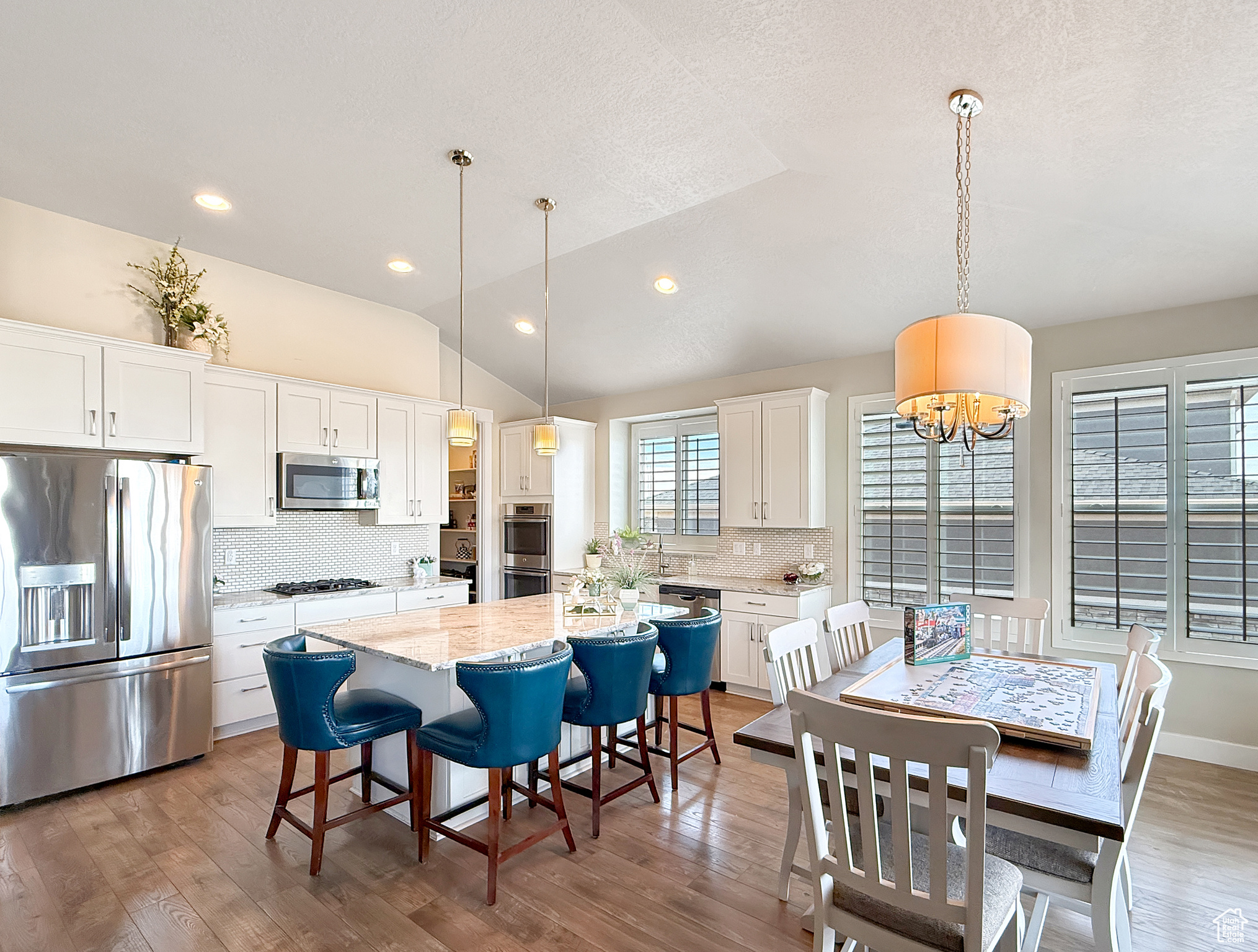 Kitchen featuring white cabinets, a kitchen island, appliances with stainless steel finishes, wood finished floors, and vaulted ceiling