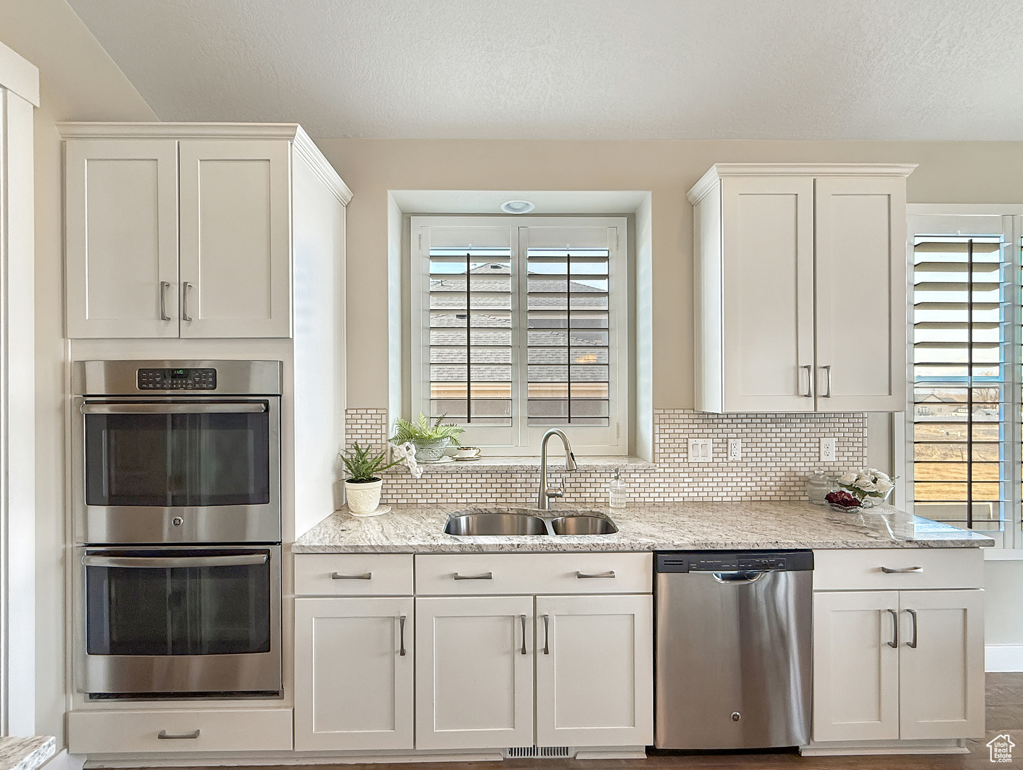 Kitchen featuring stainless steel appliances, a sink, white cabinetry, backsplash, and light stone countertops