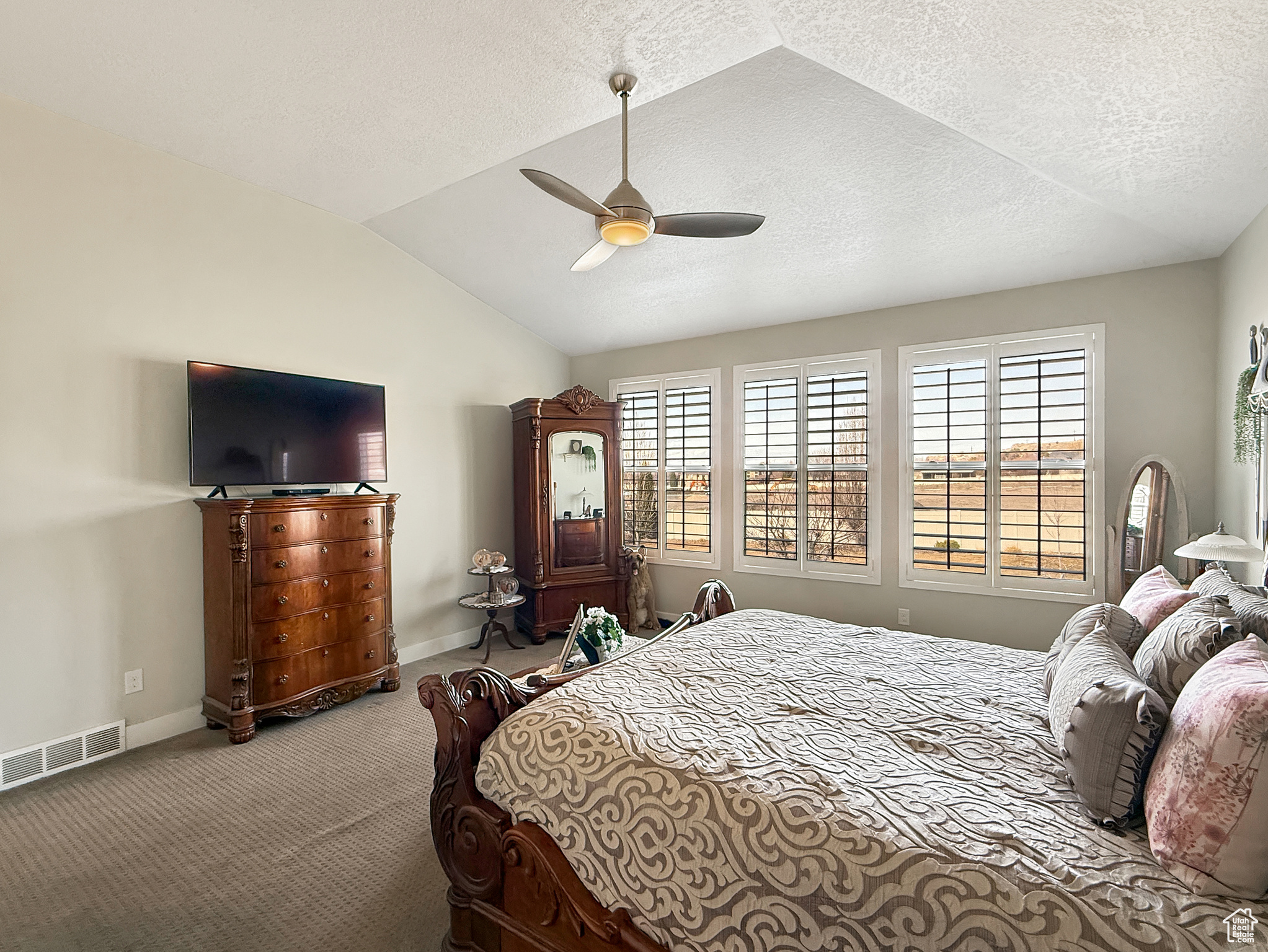 Carpeted bedroom with visible vents, vaulted ceiling, a textured ceiling, ceiling fan, and baseboards