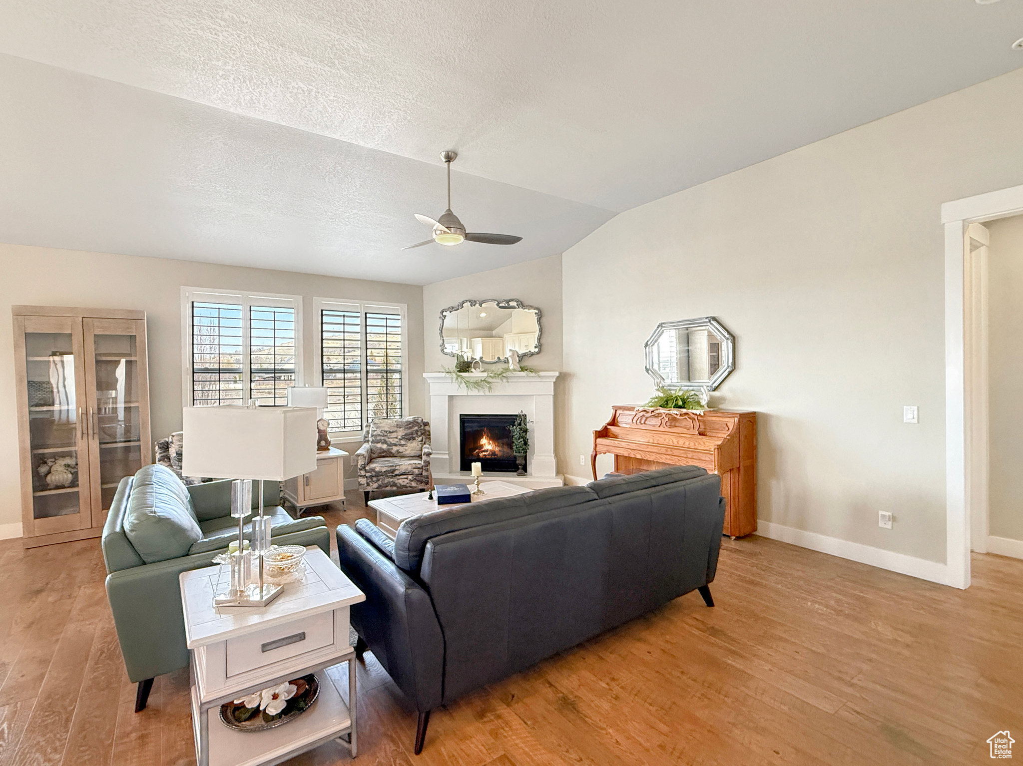 Living room featuring ceiling fan, baseboards, vaulted ceiling, a lit fireplace, and light wood-style floors