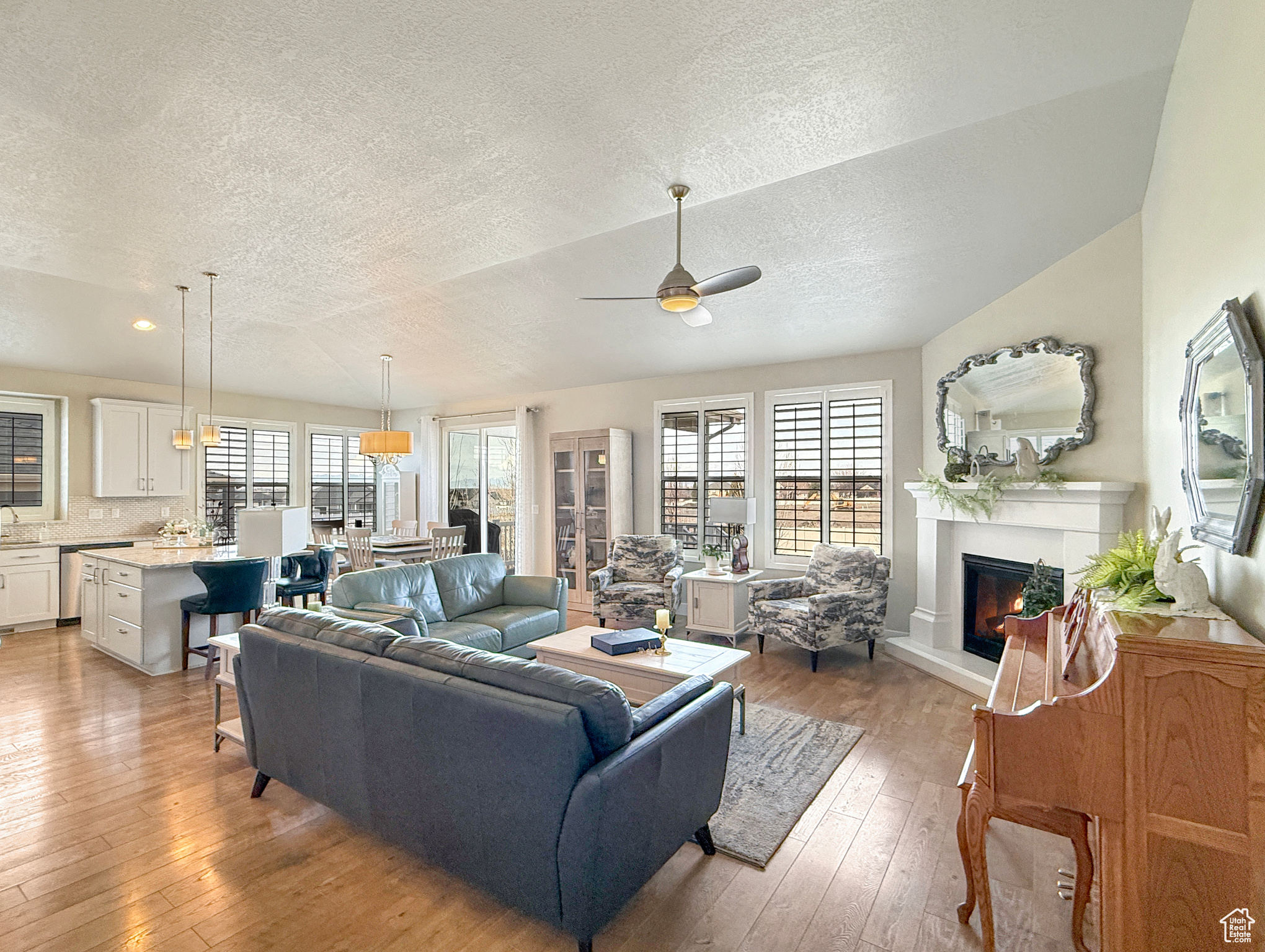 Living room featuring a ceiling fan, a glass covered fireplace, light wood-style flooring, a textured ceiling, and recessed lighting