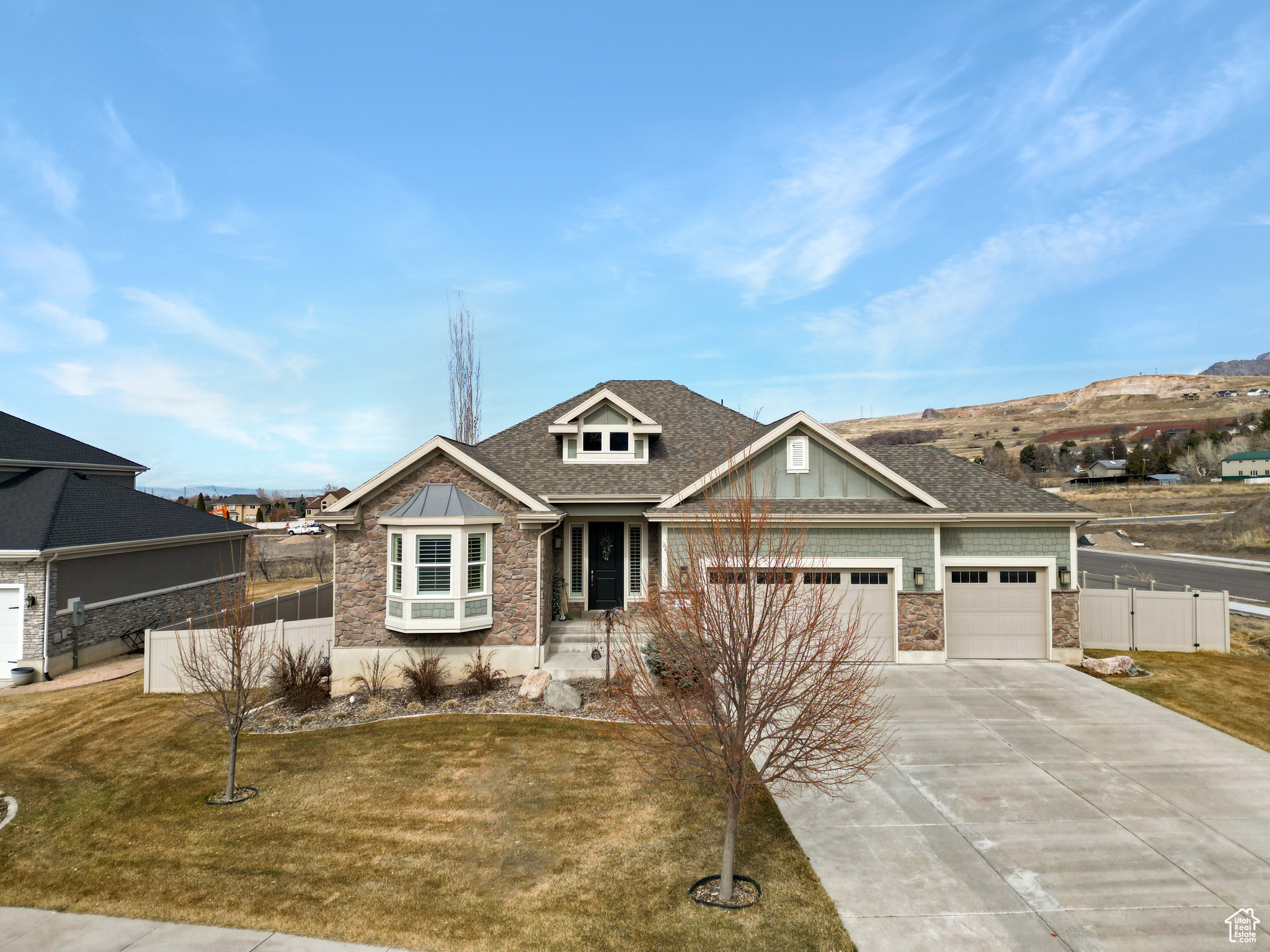 Craftsman house with a front yard, fence, a garage, stone siding, and driveway