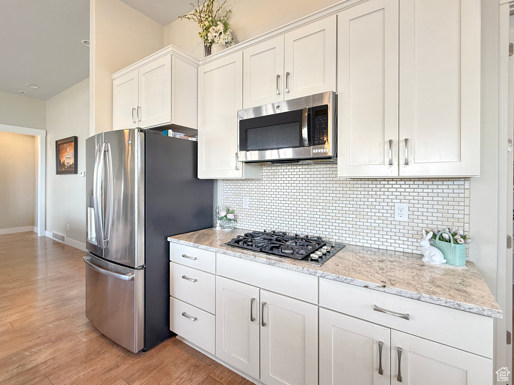 Kitchen featuring light wood finished floors, white cabinetry, appliances with stainless steel finishes, and backsplash