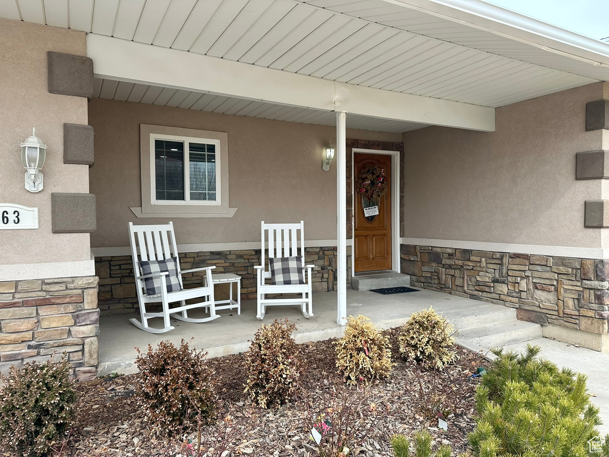 Property entrance with stone siding, a porch, and stucco siding