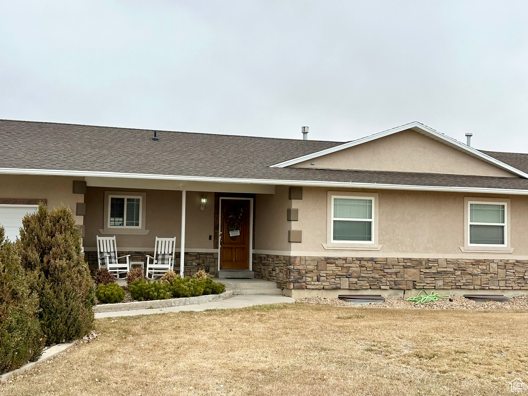 View of front of property featuring stone siding, a shingled roof, a porch, and stucco siding