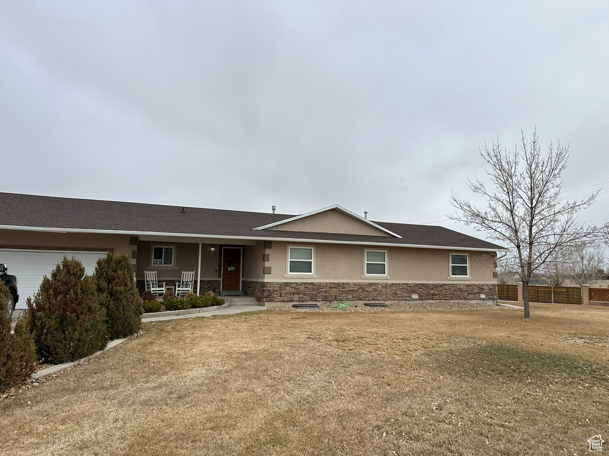 Single story home featuring stone siding, a porch, fence, and stucco siding