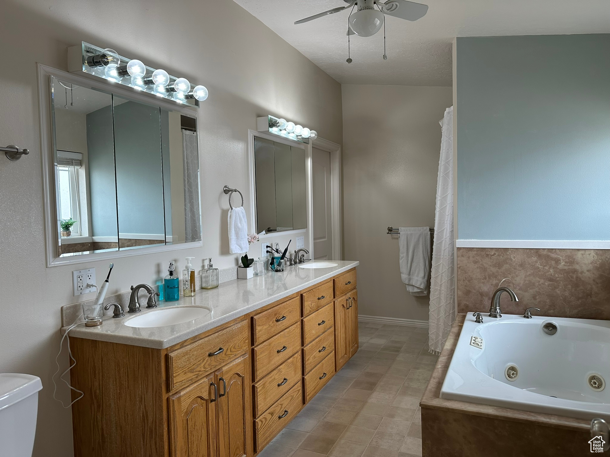 Full bathroom featuring a whirlpool tub, double vanity, ceiling fan, and a sink