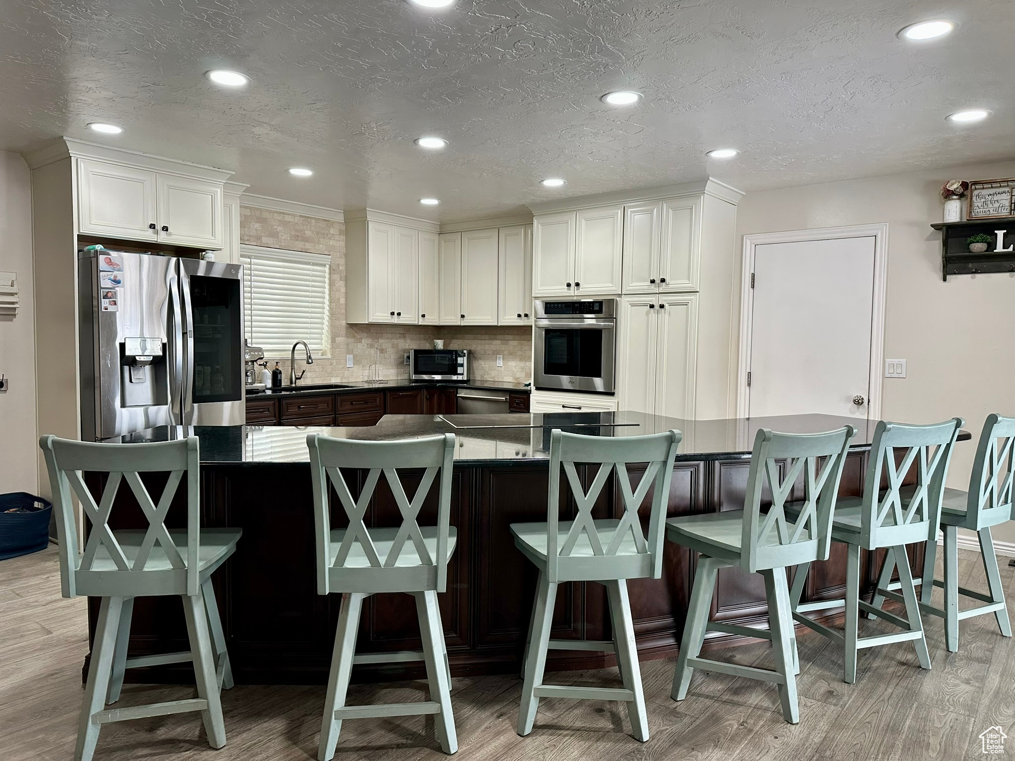 Kitchen featuring stainless steel appliances, light wood-style flooring, decorative backsplash, white cabinets, and a sink