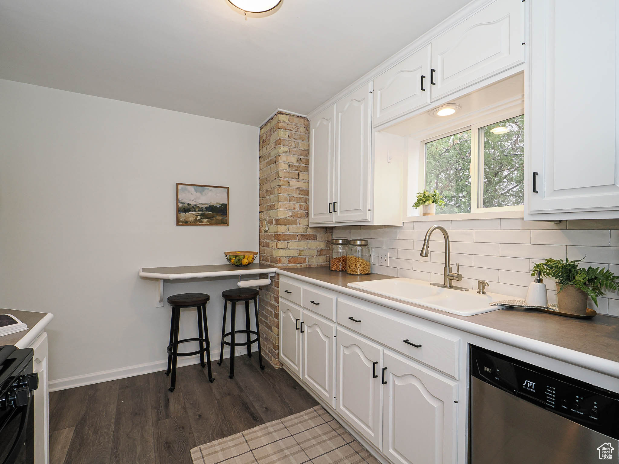 Kitchen featuring dark wood finished floors, decorative backsplash, white cabinetry, a sink, and dishwasher