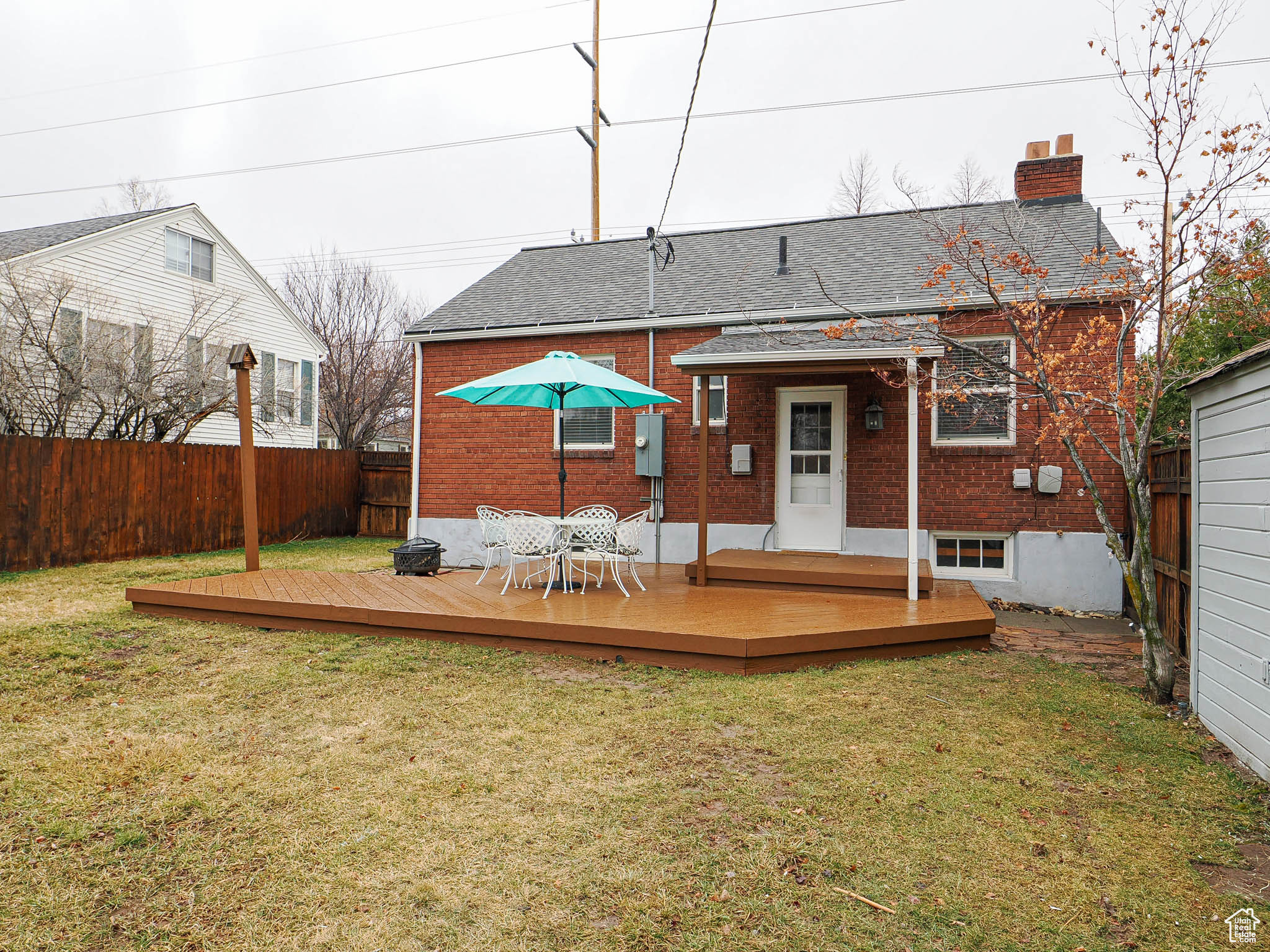 Back of property featuring a lawn, a fenced backyard, a chimney, a wooden deck, and brick siding