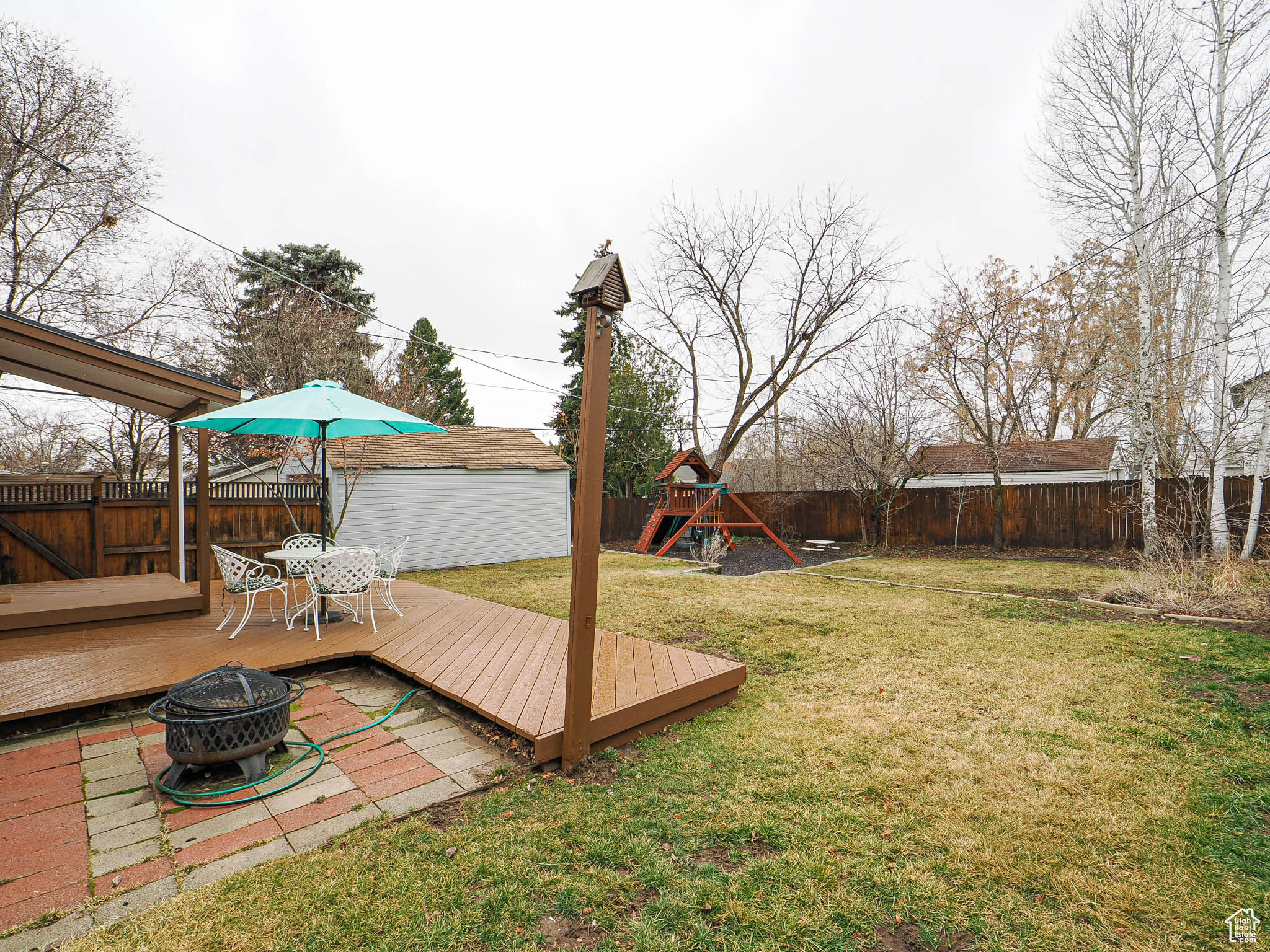 View of yard featuring a playground, an outdoor fire pit, a fenced backyard, an outdoor structure, and a wooden deck