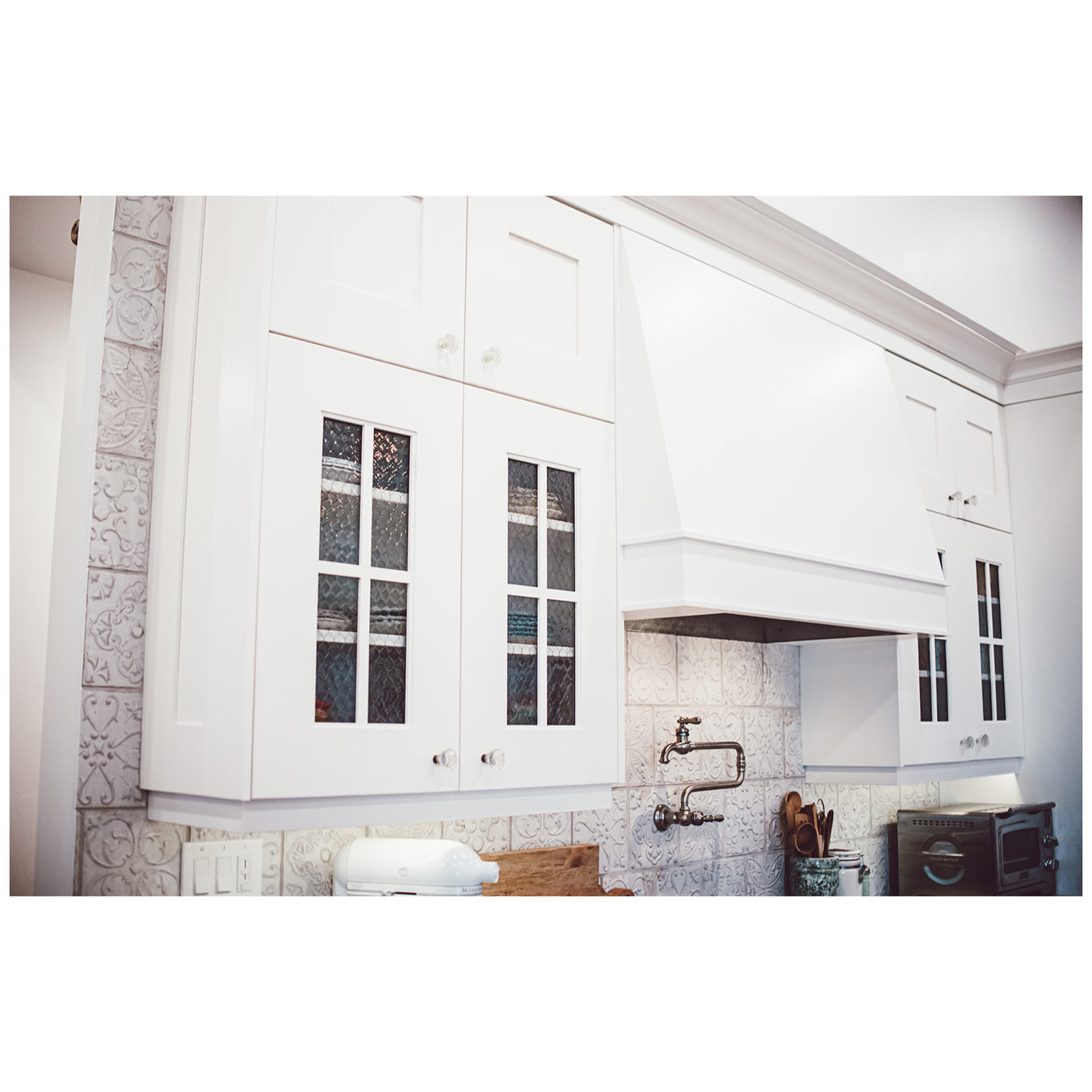 Kitchen with glass insert cabinets, tasteful backsplash, premium range hood, and white cabinetry