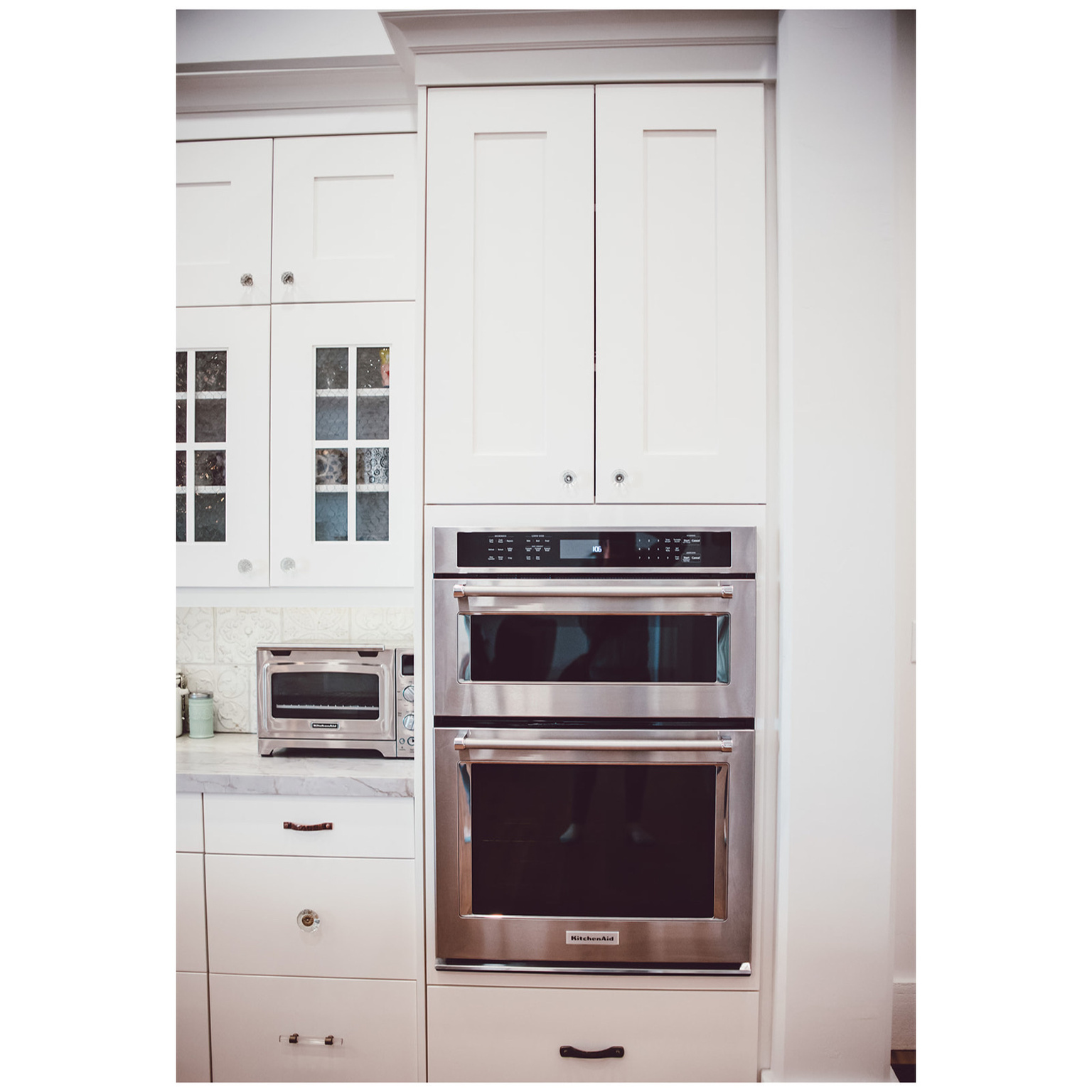 Kitchen featuring a toaster, tasteful backsplash, glass insert cabinets, stainless steel double oven, and white cabinets