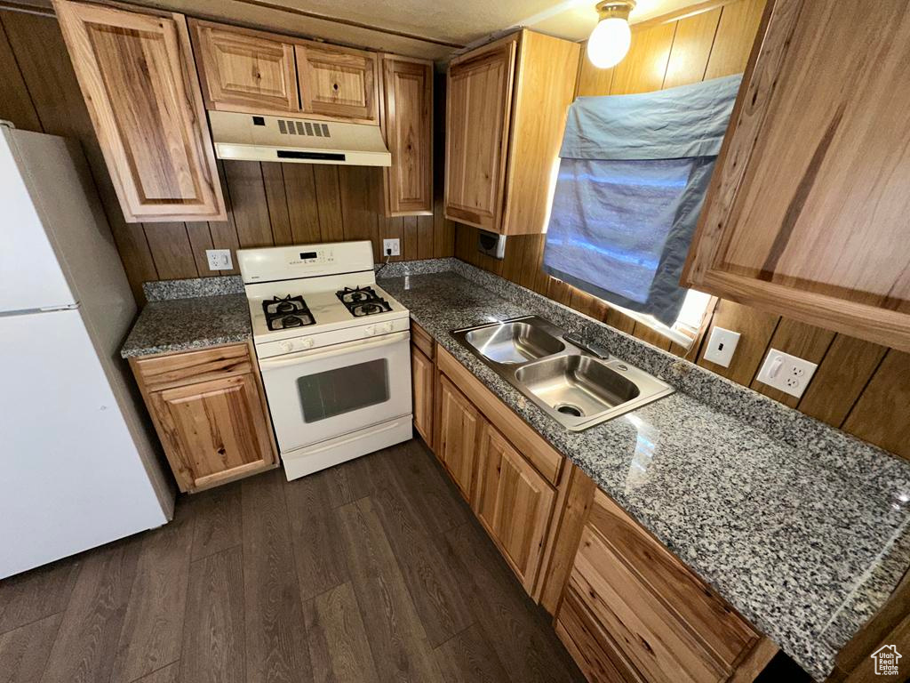 Kitchen with white appliances, brown cabinets, dark wood-type flooring, under cabinet range hood, and a sink