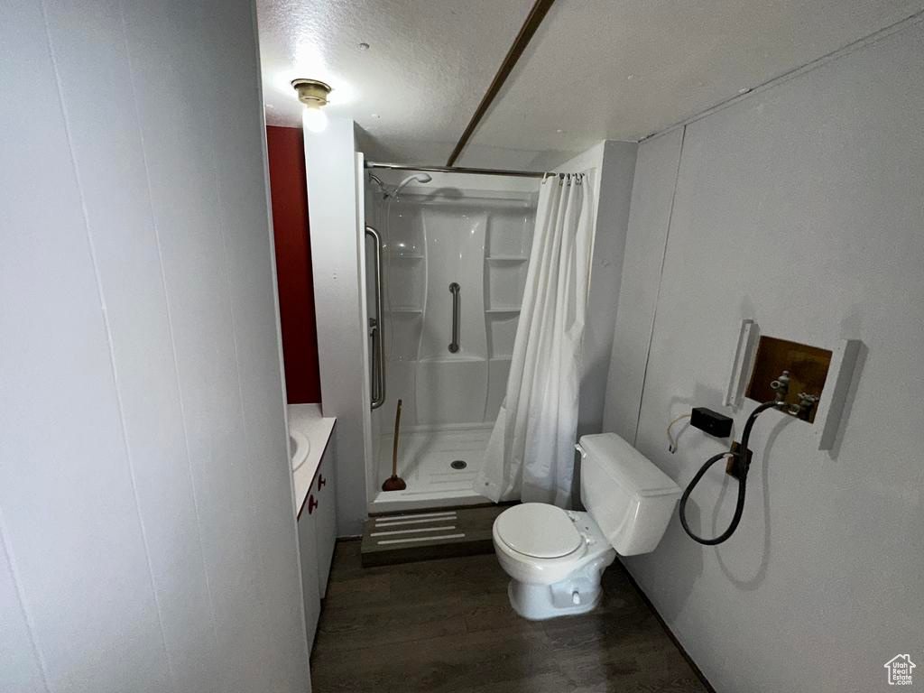 Bathroom with a textured ceiling, toilet, a decorative wall, wood finished floors, and a stall shower