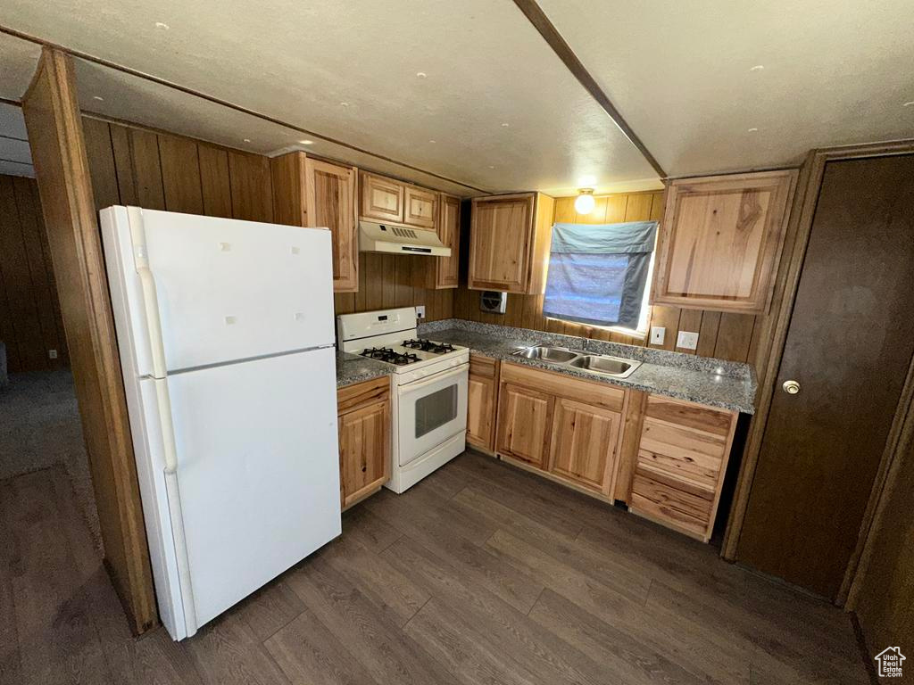 Kitchen featuring white appliances, dark wood-style flooring, wood walls, under cabinet range hood, and a sink