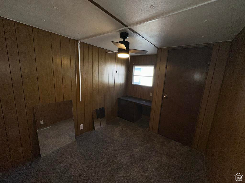 Carpeted empty room with wooden walls, built in desk, and a ceiling fan