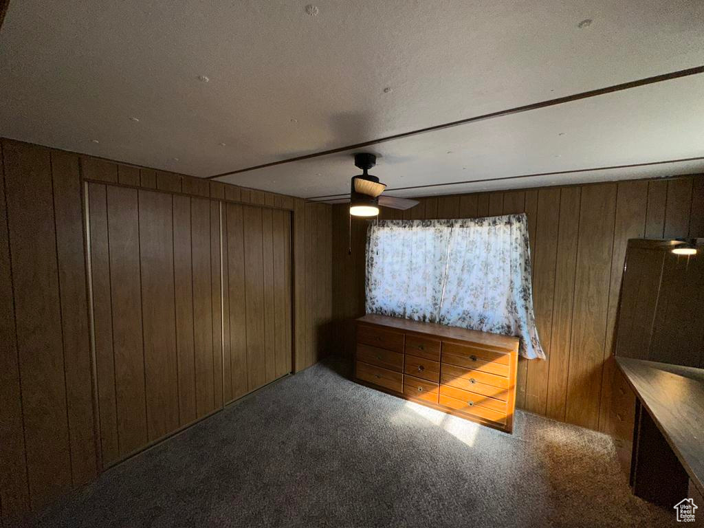 Unfurnished bedroom featuring ceiling fan, carpet, and wooden walls