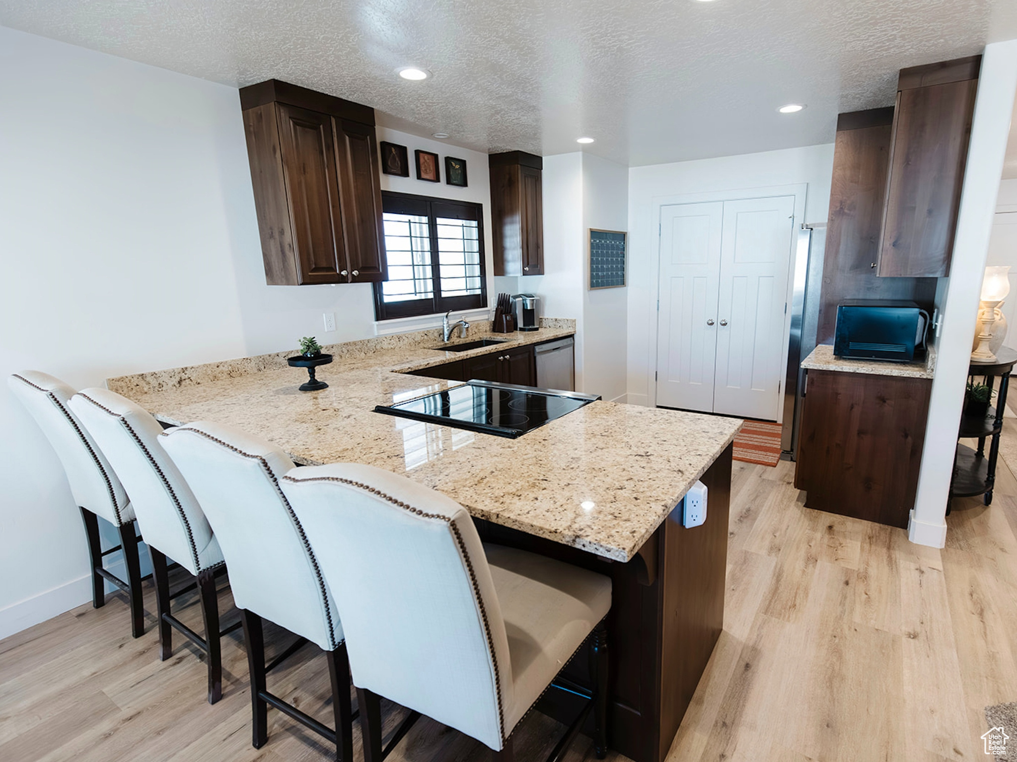 Kitchen with dark brown cabinets, a peninsula, a kitchen bar, and light wood-style flooring