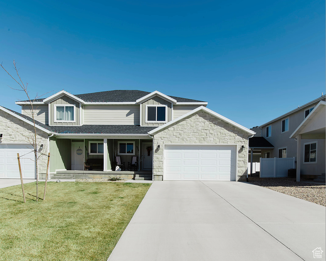 Traditional home with a porch, a garage, fence, concrete driveway, and a front lawn