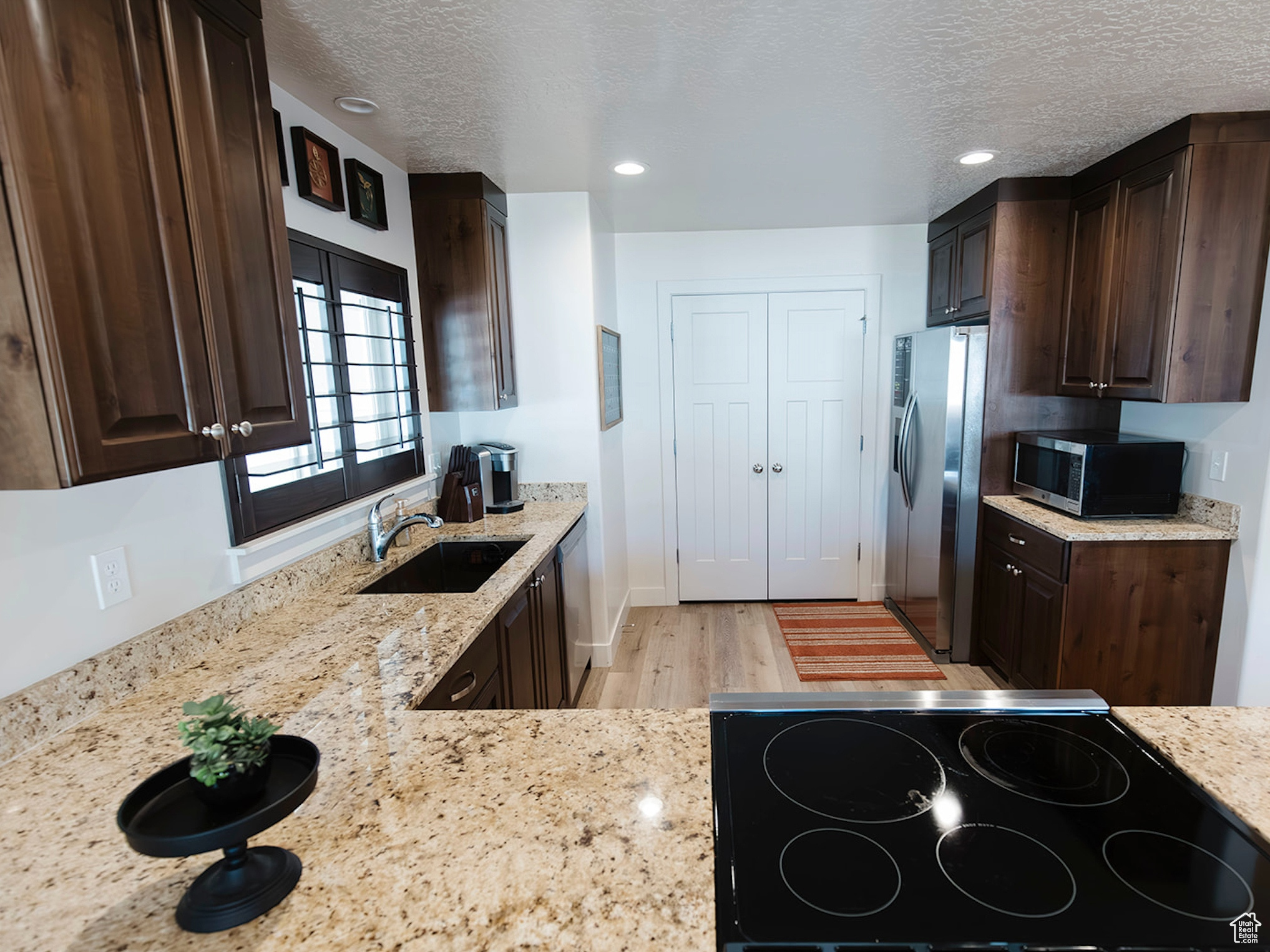 Kitchen featuring dark brown cabinetry, appliances with stainless steel finishes, light stone countertops, a textured ceiling, and a sink