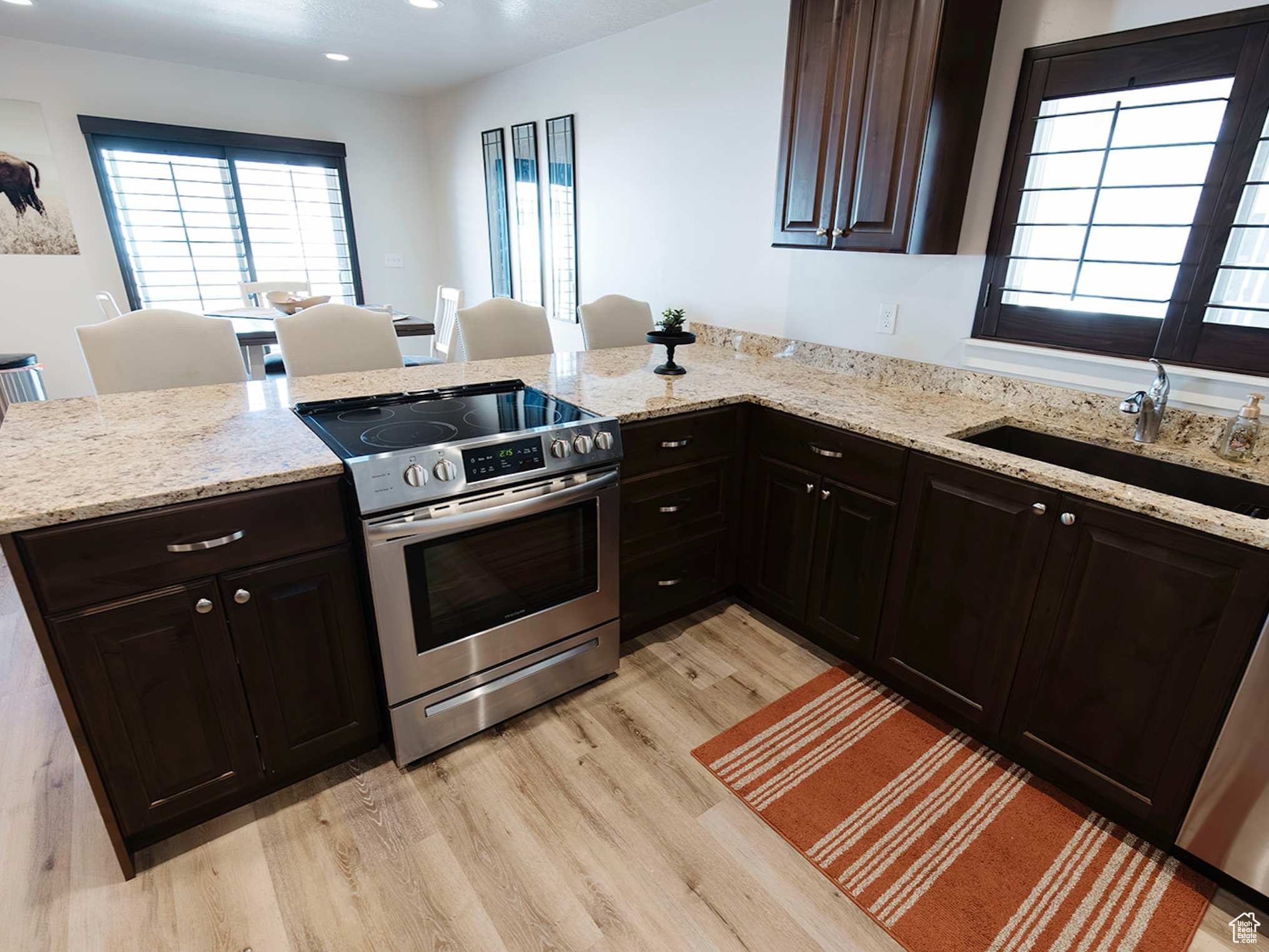 Kitchen with light stone counters, stainless steel appliances, a peninsula, a sink, and light wood finished floors