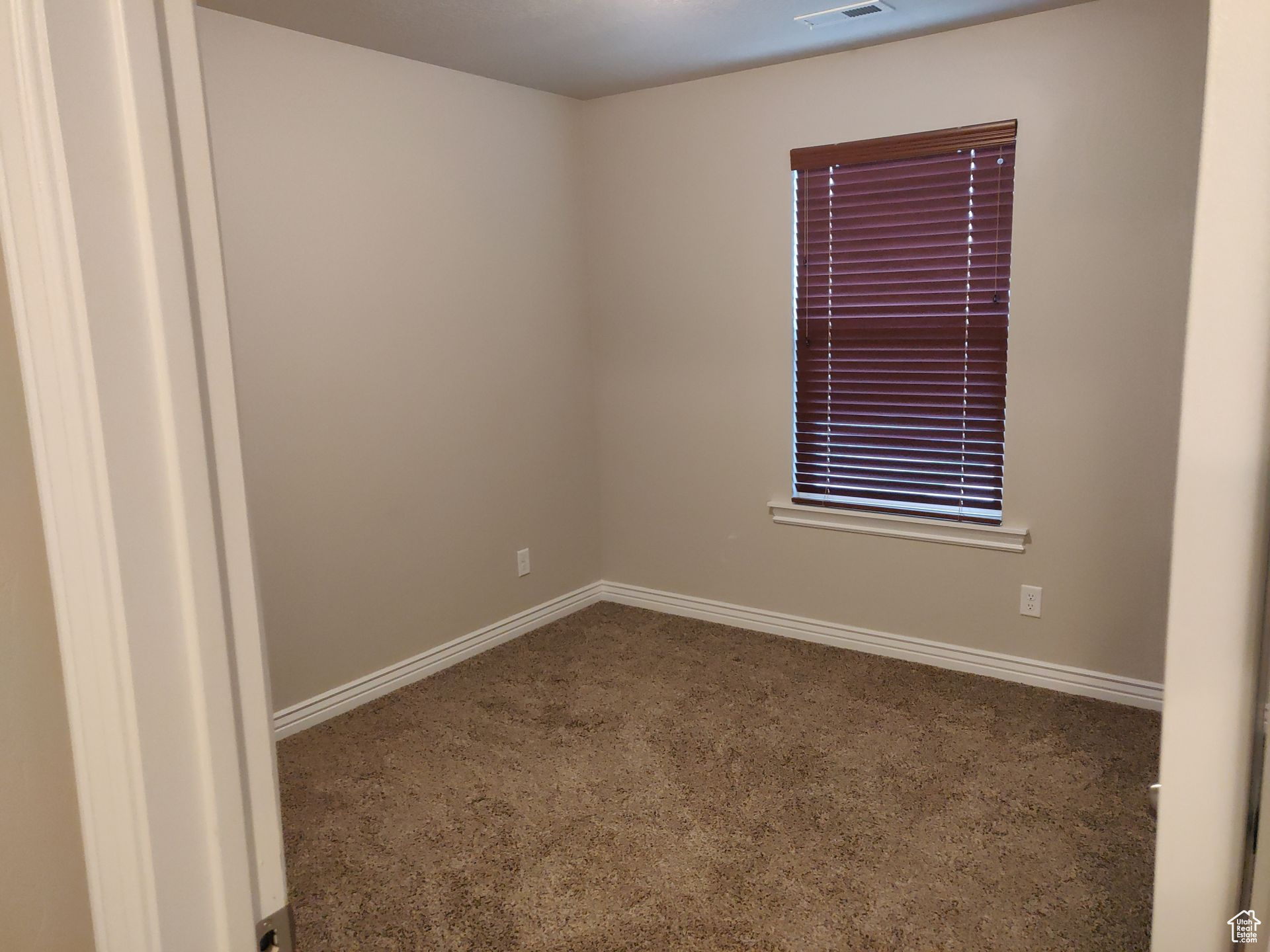 Empty room with carpet flooring, visible vents, and baseboards