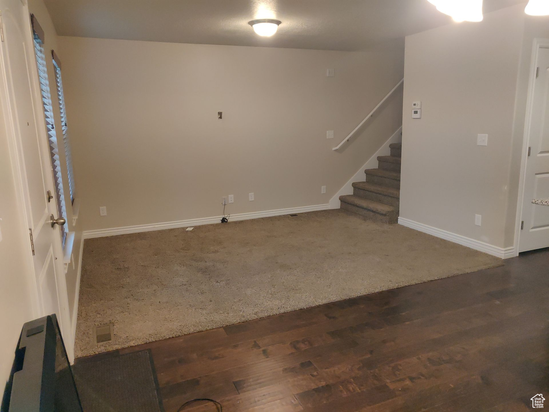 Carpeted empty room with baseboards, wood finished floors, and stairs