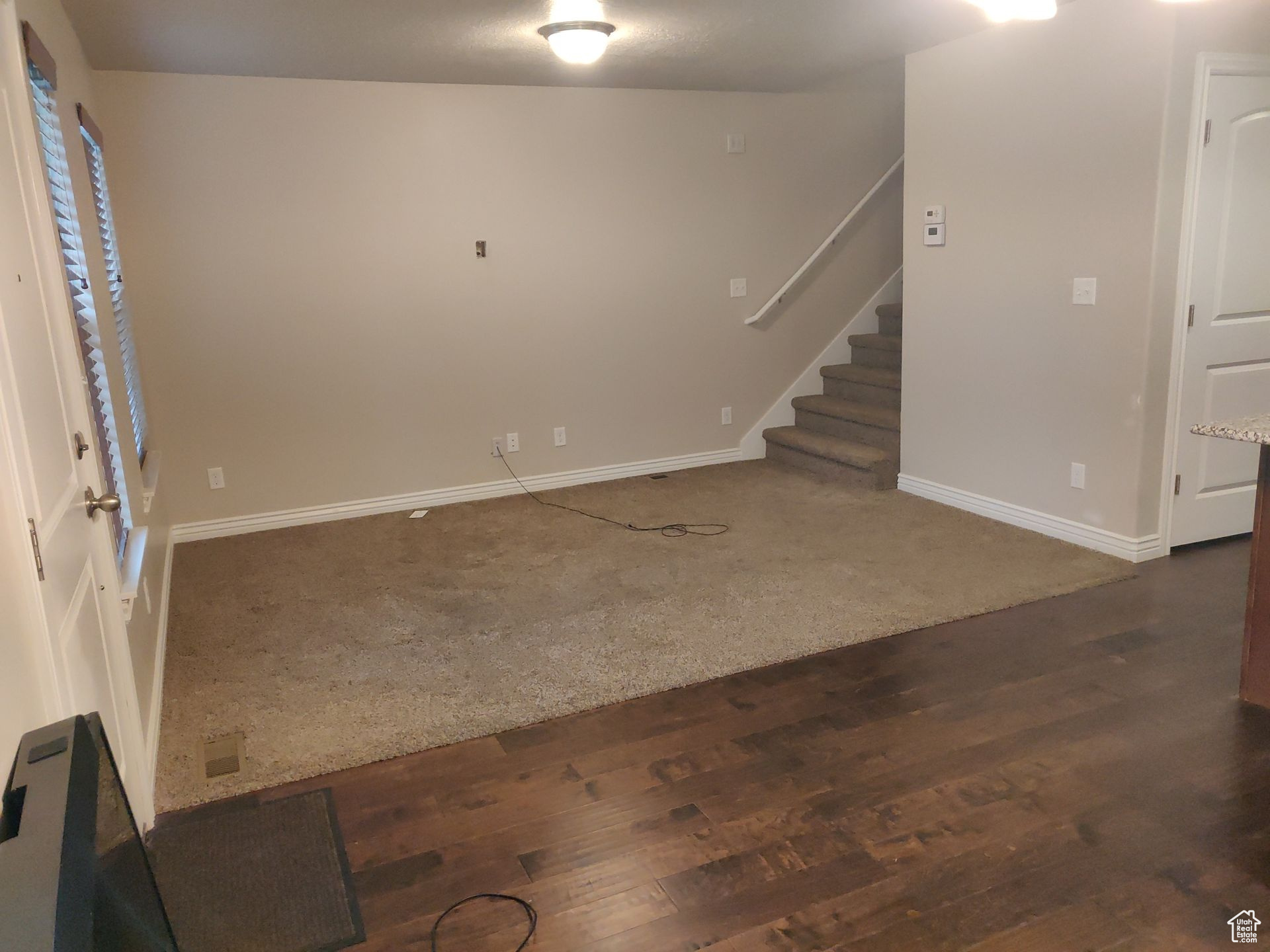 Empty room featuring dark wood-type flooring, stairway, baseboards, and dark carpet