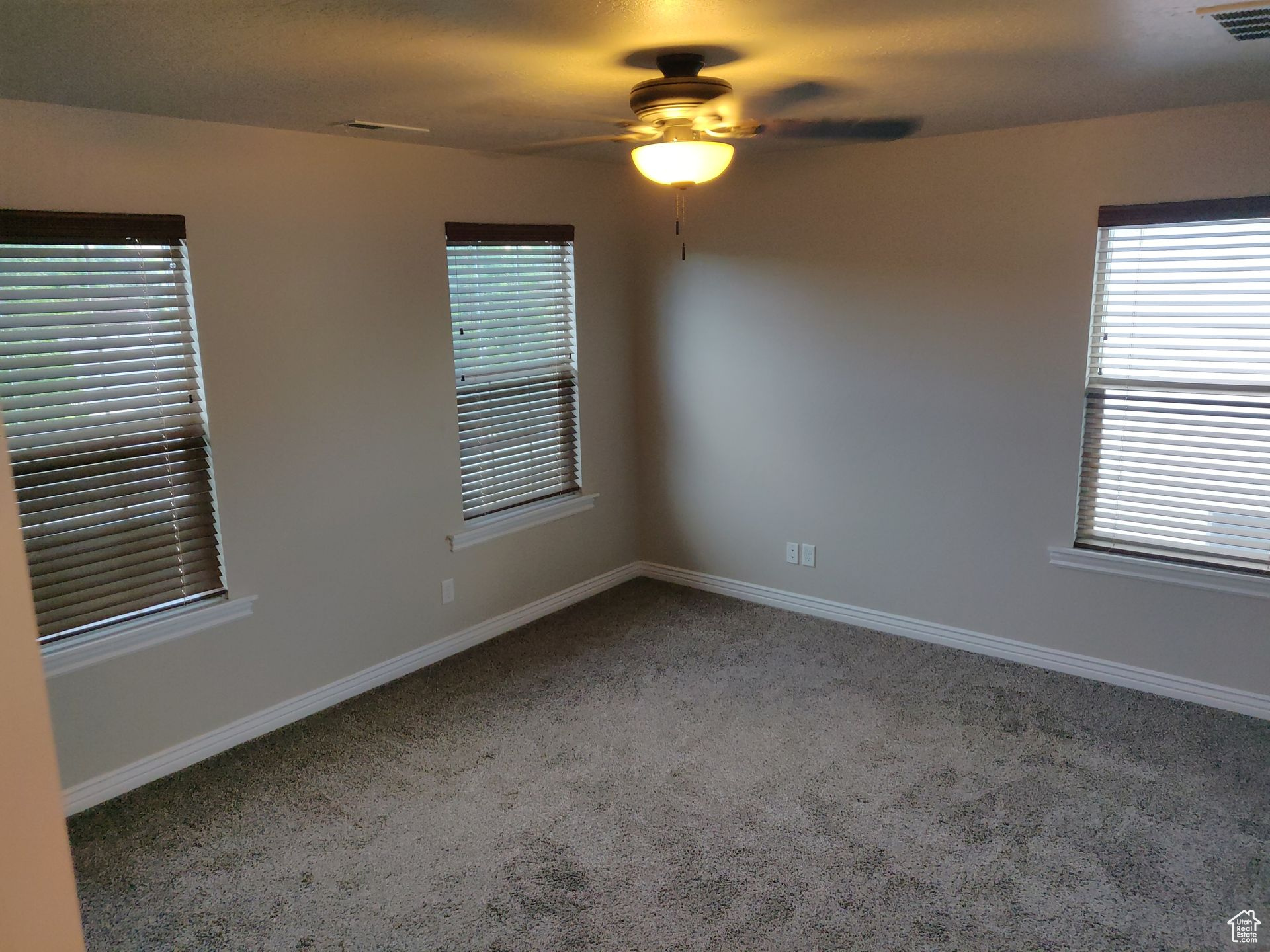 Carpeted spare room with visible vents, baseboards, and a ceiling fan