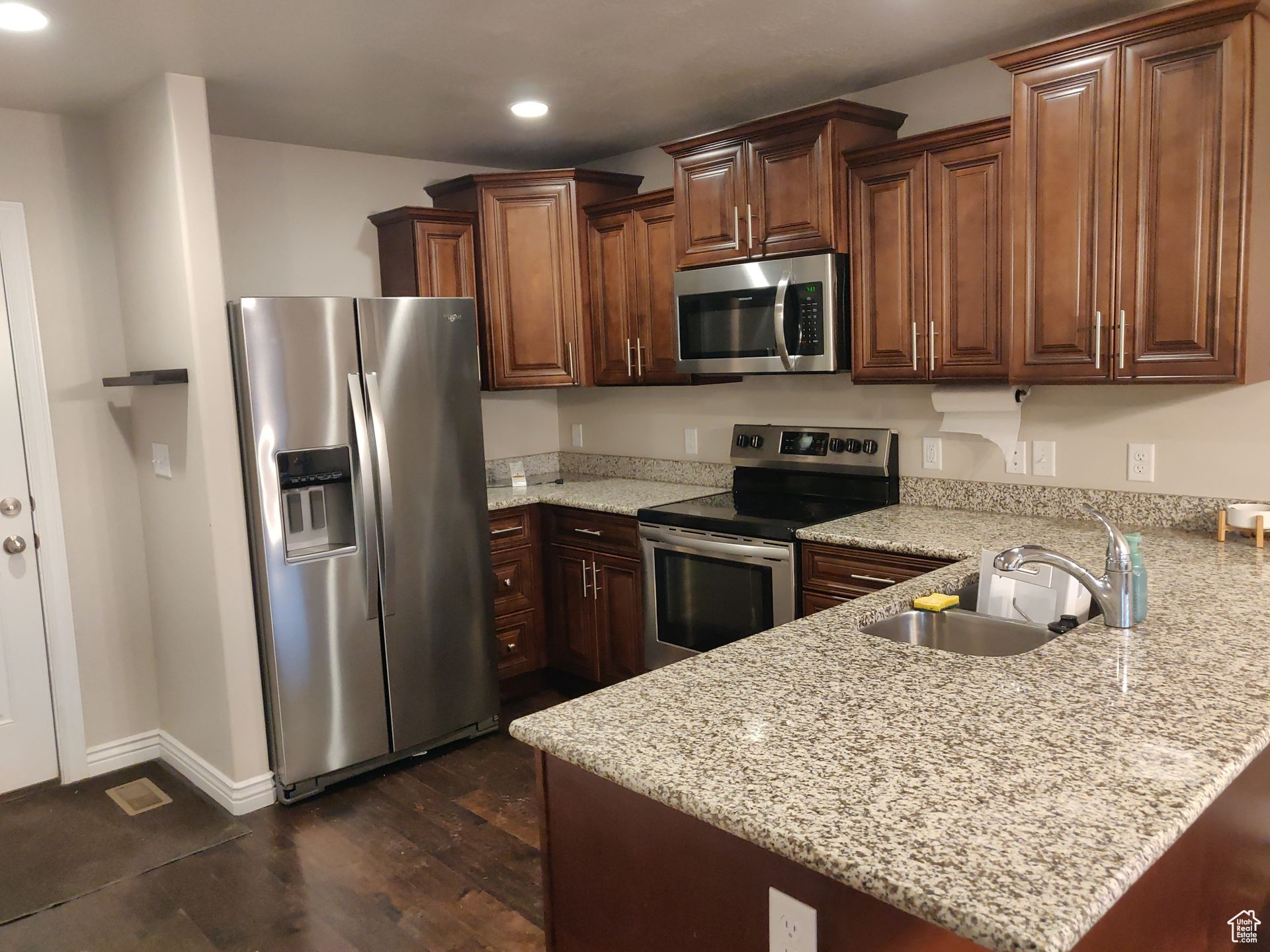 Kitchen with light stone counters, a peninsula, recessed lighting, a sink, and appliances with stainless steel finishes