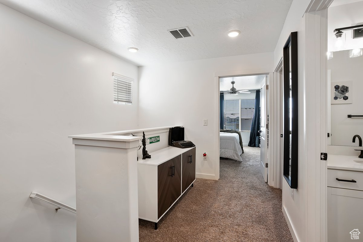 Corridor with baseboards, carpet, visible vents, and a textured ceiling