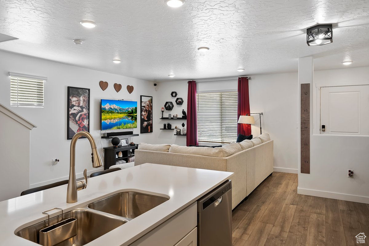 Kitchen with light countertops, dark wood-style flooring, stainless steel dishwasher, a textured ceiling, and a sink