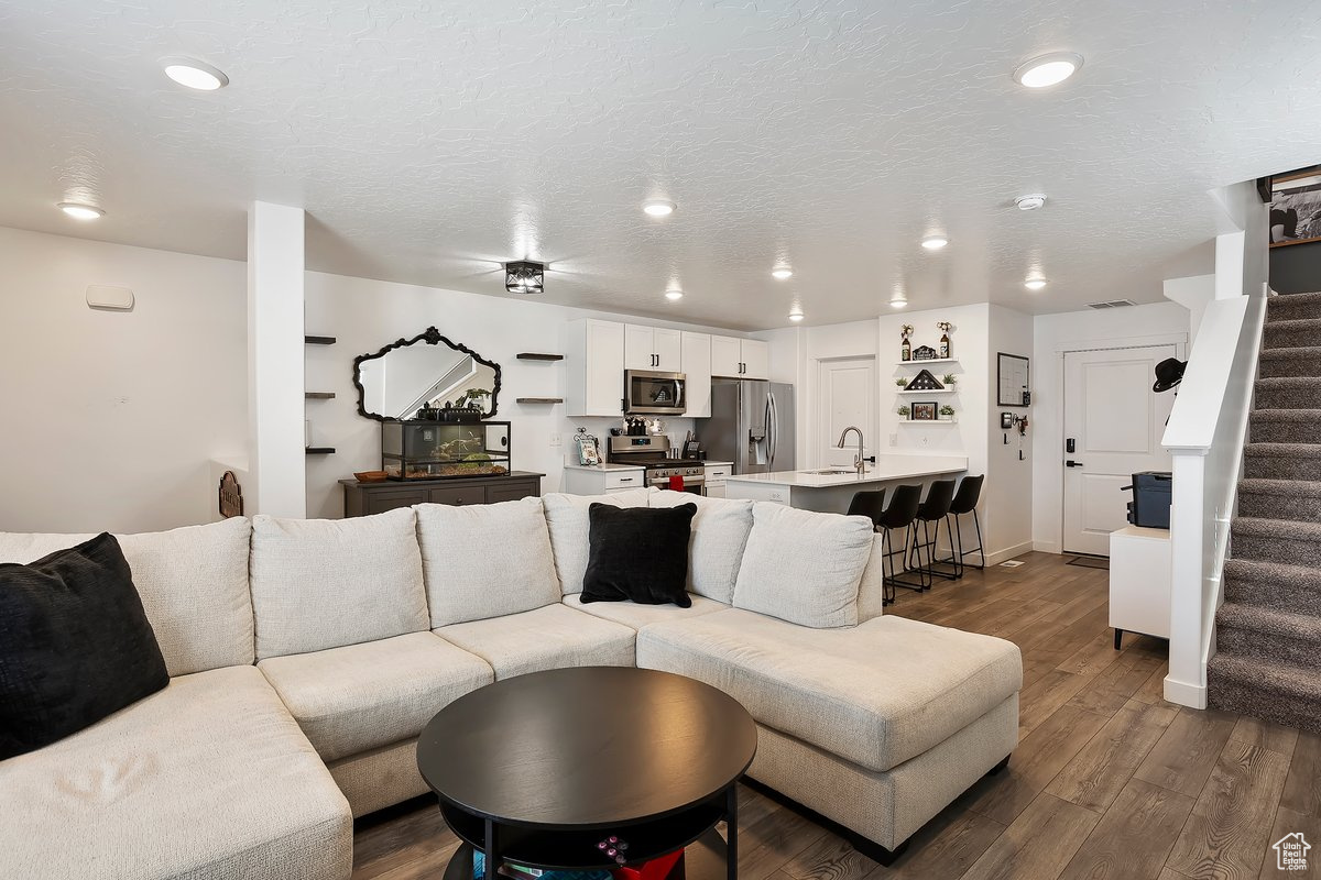 Living area with stairway, recessed lighting, a textured ceiling, and dark wood-style flooring