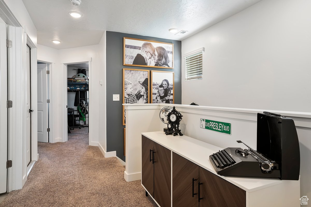 Hallway featuring light carpet, a textured ceiling, and baseboards