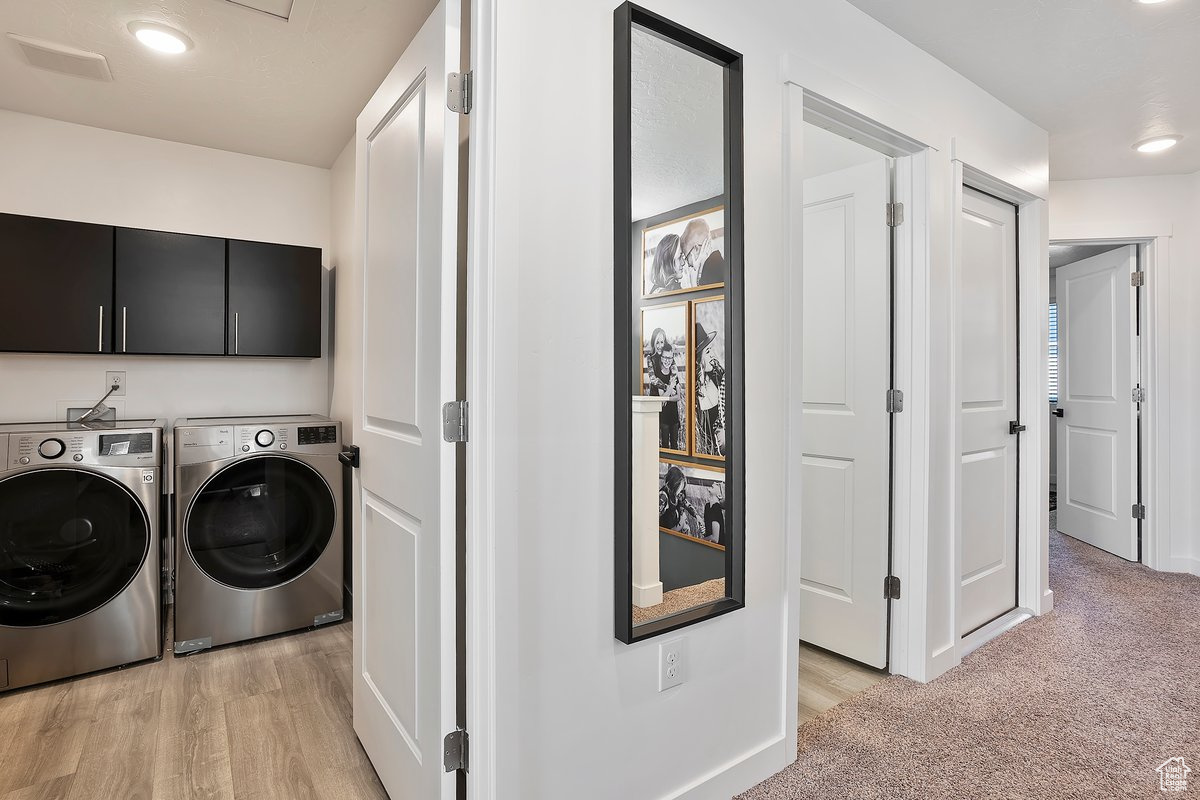 Washroom with cabinet space, washer and dryer, light colored carpet, and light wood-type flooring