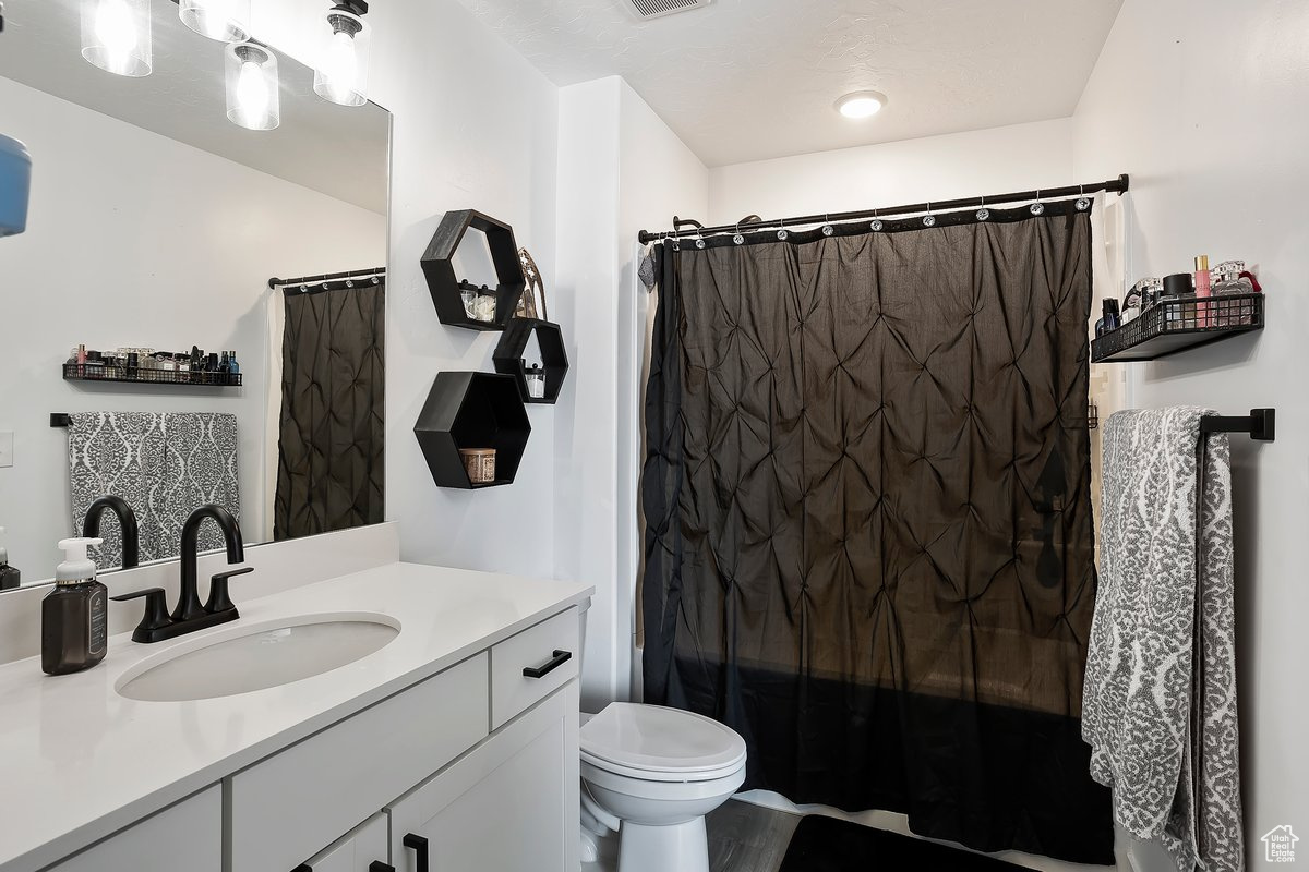 Full bathroom with vanity, curtained shower, toilet, and visible vents