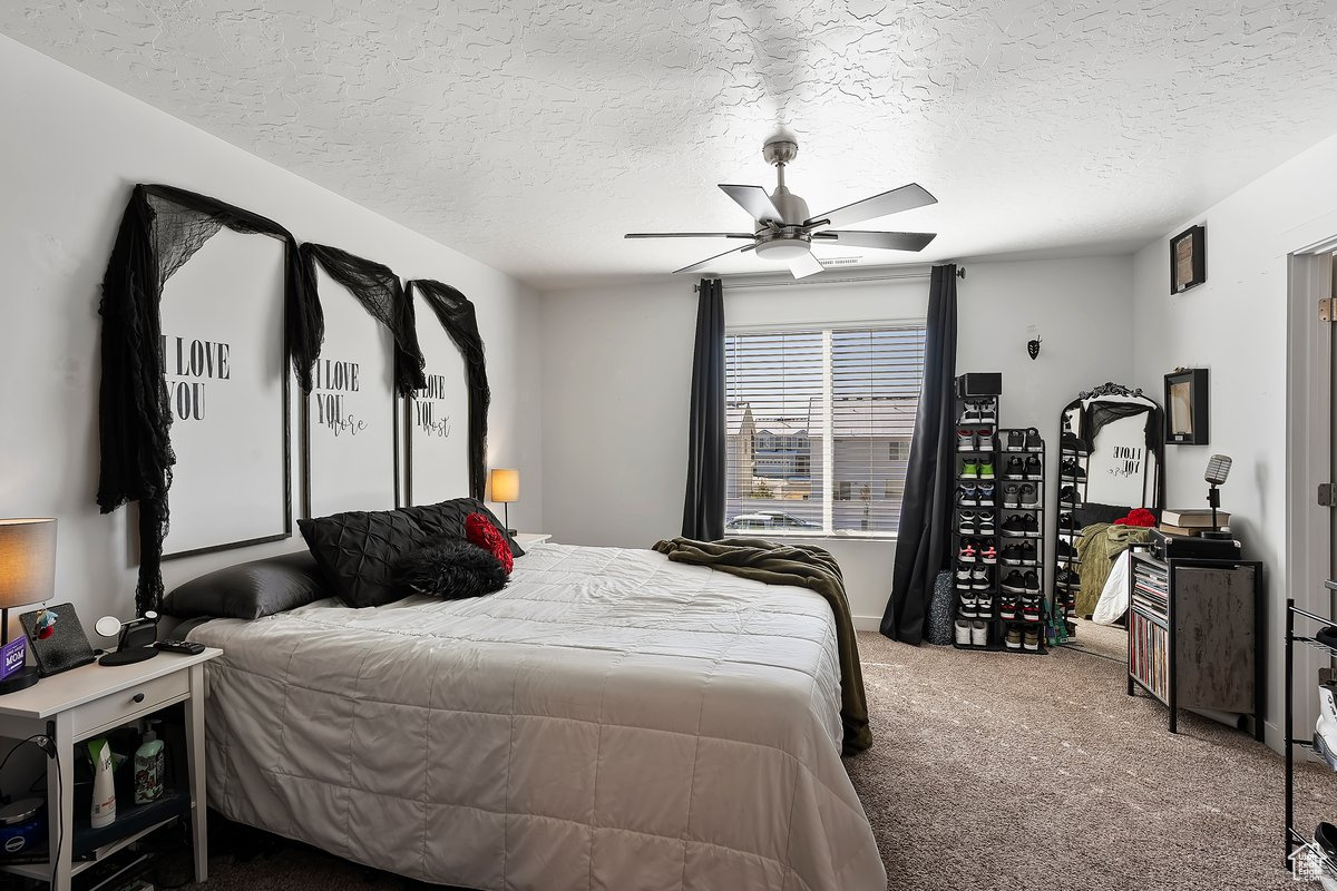 Carpeted bedroom featuring ceiling fan and a textured ceiling