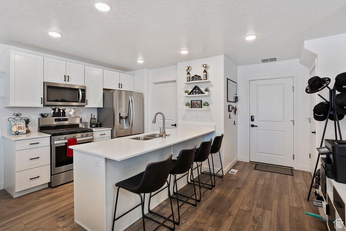 Kitchen with visible vents, a breakfast bar, appliances with stainless steel finishes, dark wood-style floors, and a sink