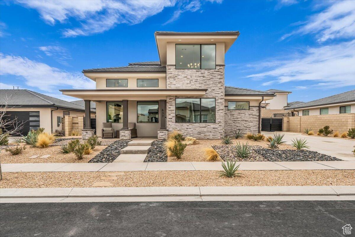 View of front of property with fence, covered porch, stucco siding, stone siding, and driveway