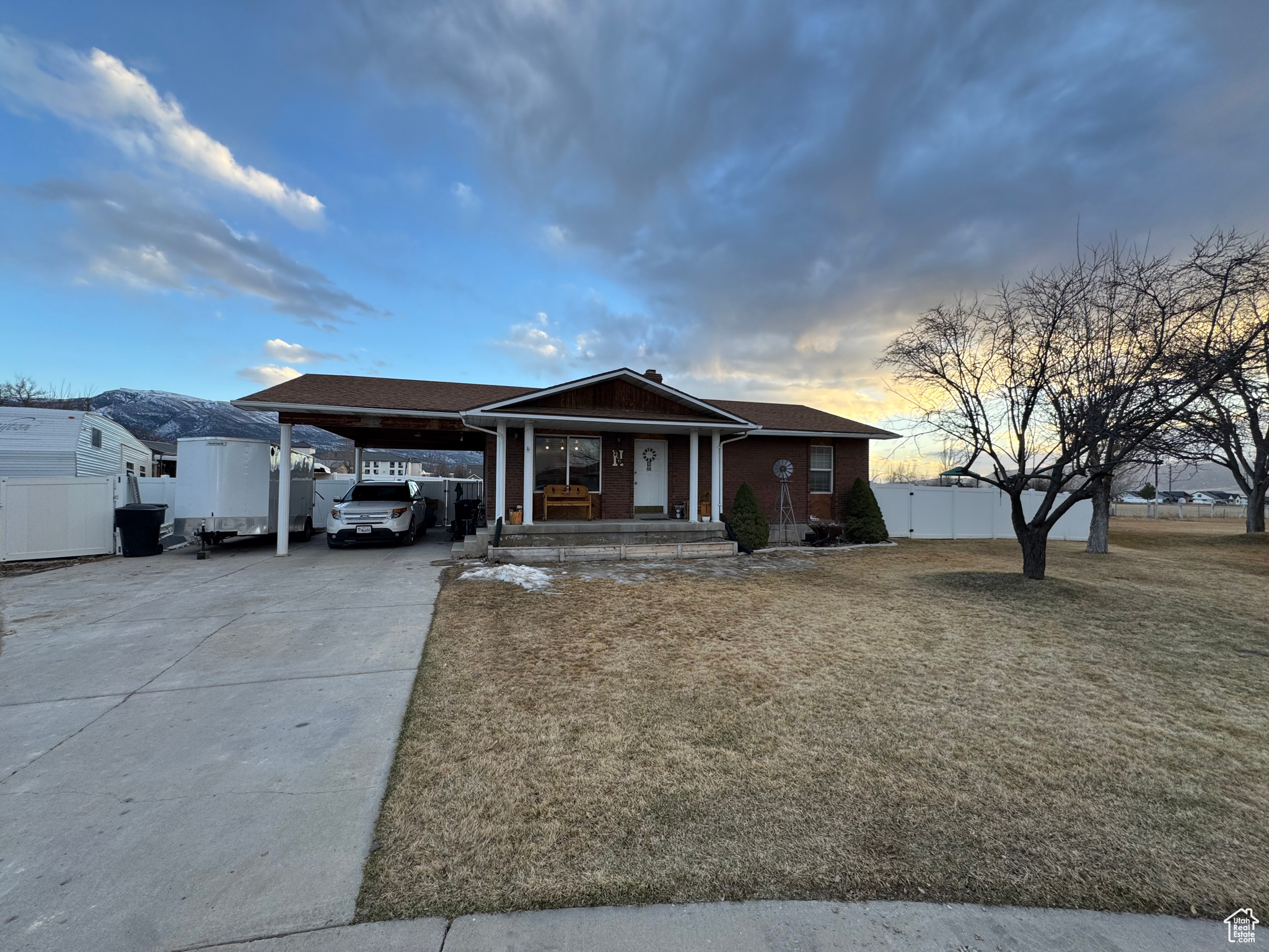 View of front of home with brick siding, a front lawn, fence, concrete driveway, and a carport