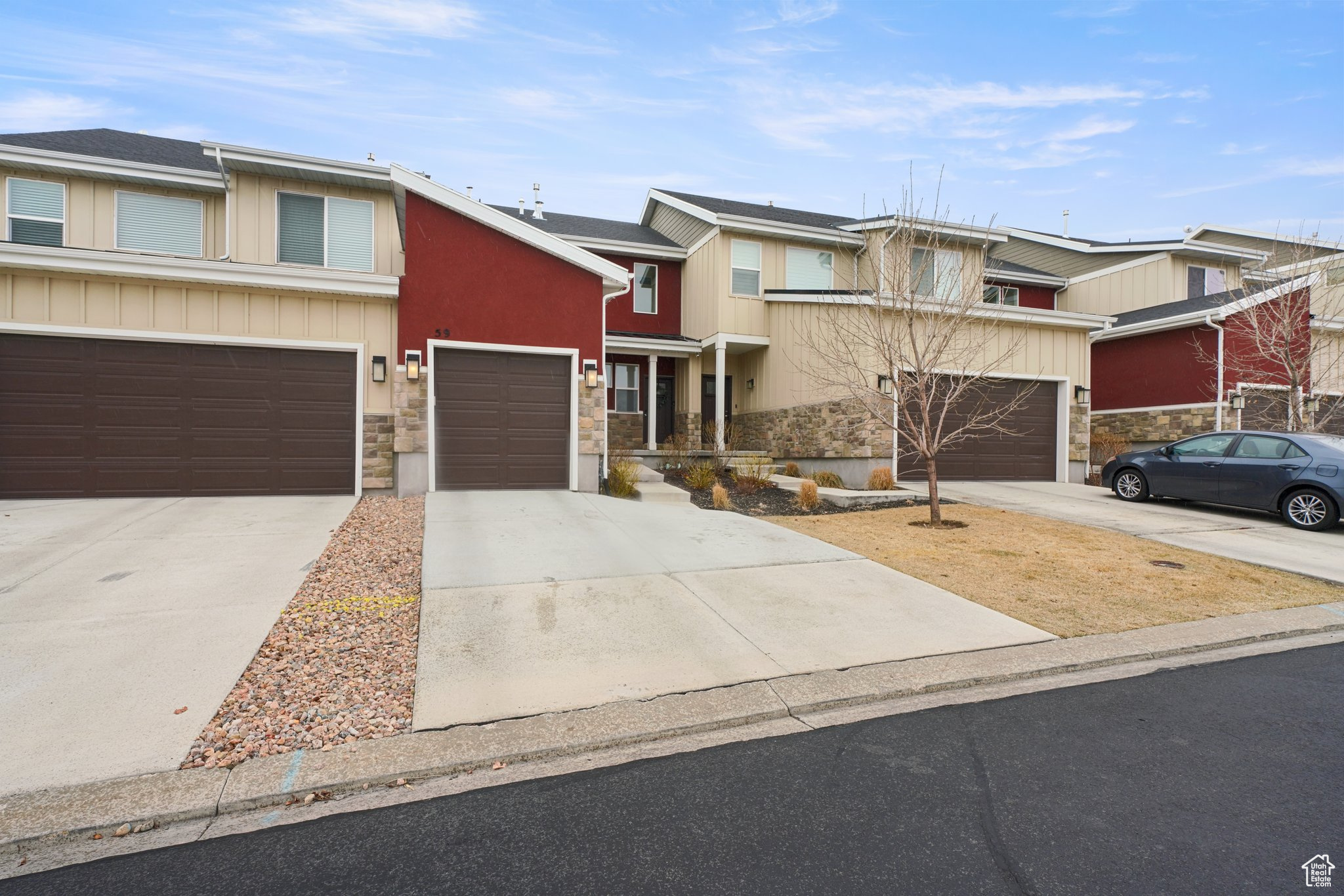 Multi unit property featuring stone siding, driveway, a garage, and roof mounted solar panels