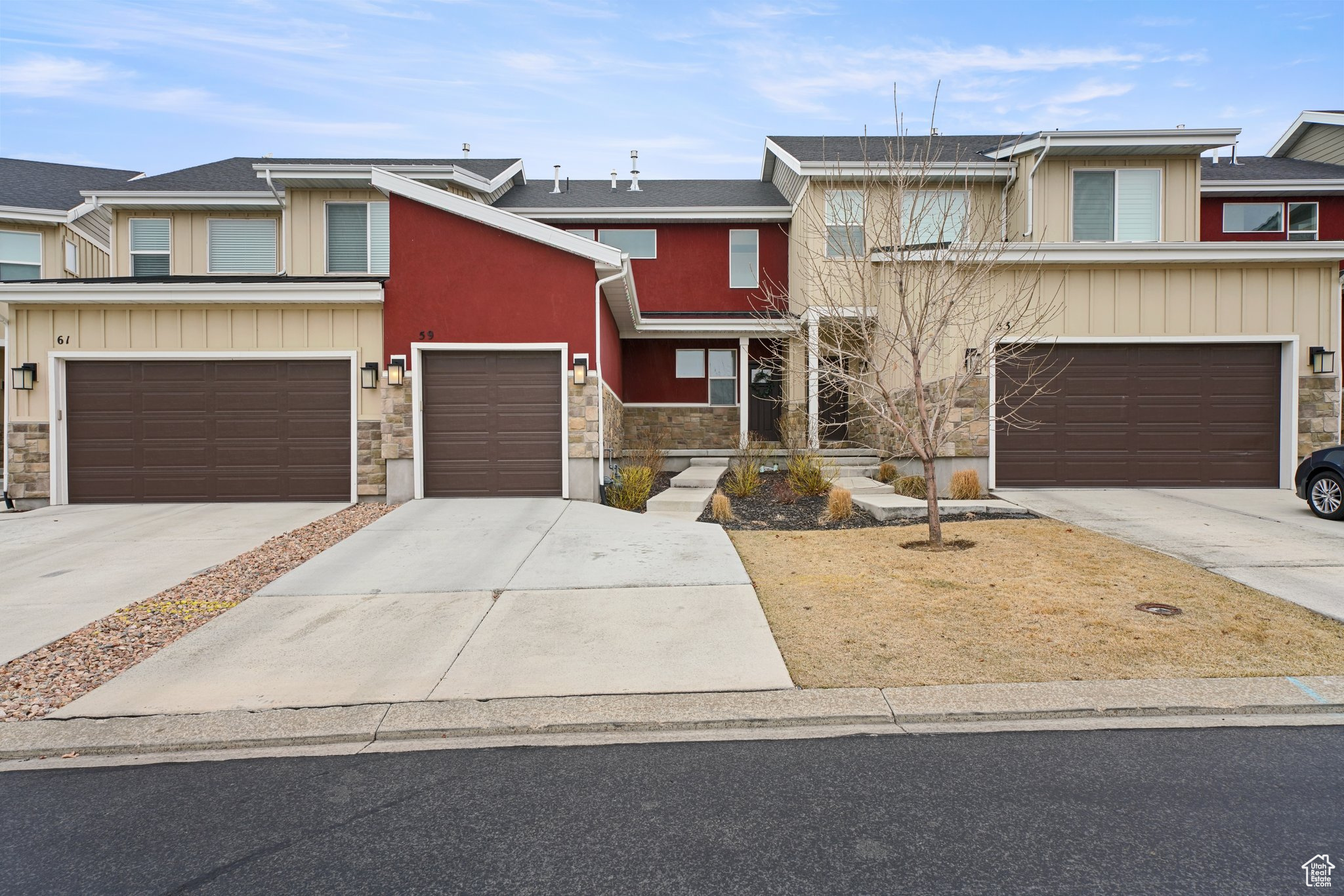 Townhome / multi-family property with solar panels, stone siding, and driveway